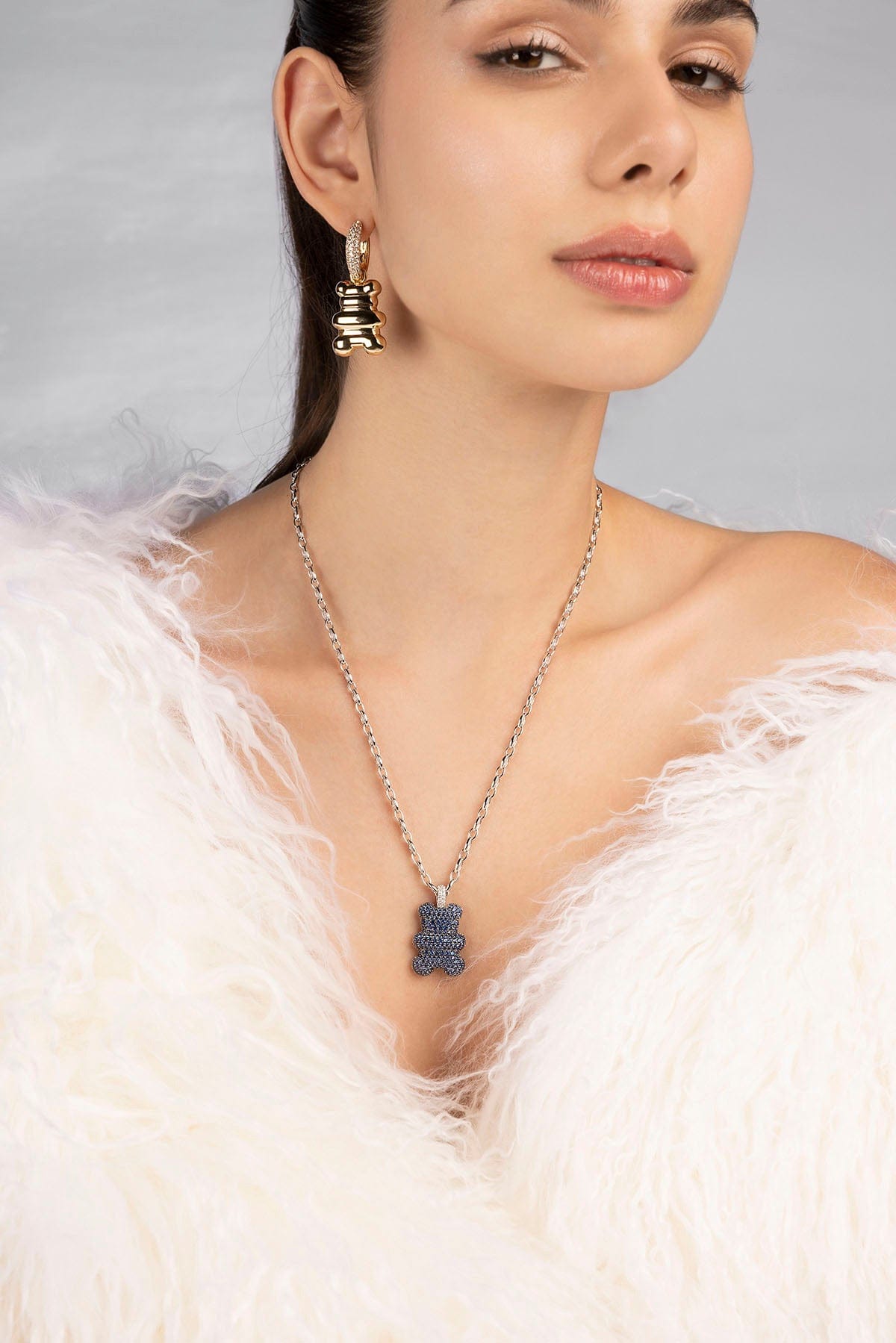 Woman wearing a necklace with a pendant and earrings against a neutral background