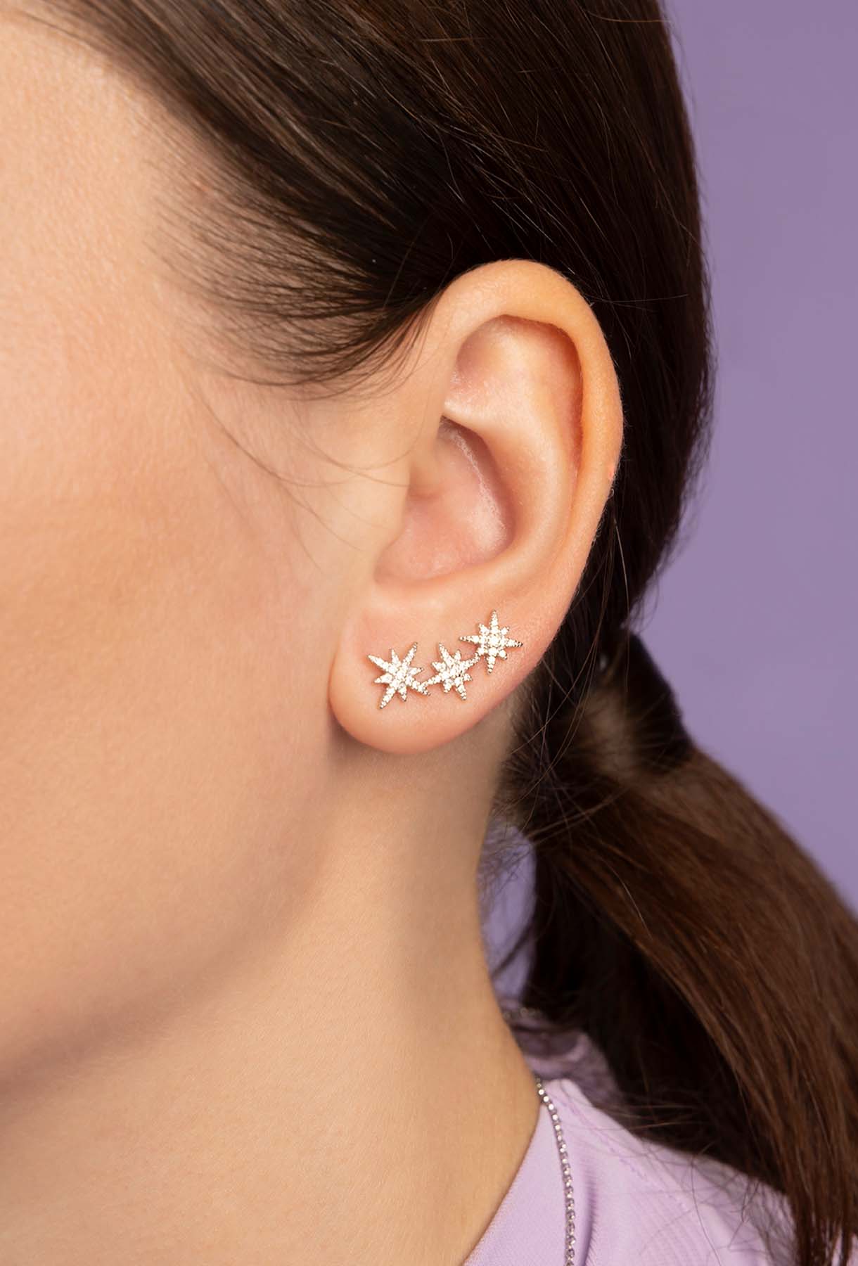 Close-up of an ear wearing star-shaped earrings with a blurred background