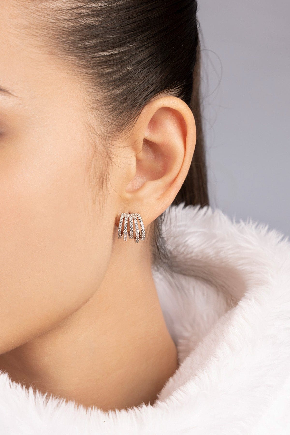 Close-up of a person wearing five-hoop silver earrings from APM MONACO with a blurred background