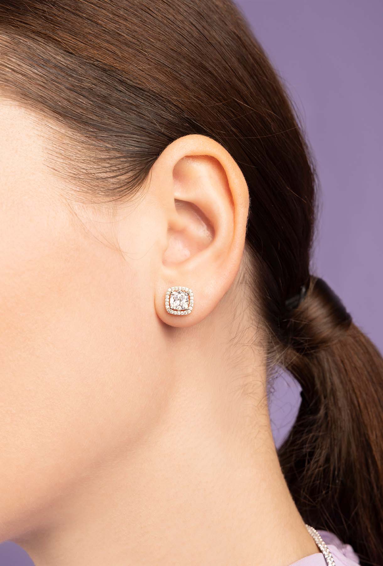 Close-up of a person wearing zirconia stud earrings with a blurred background