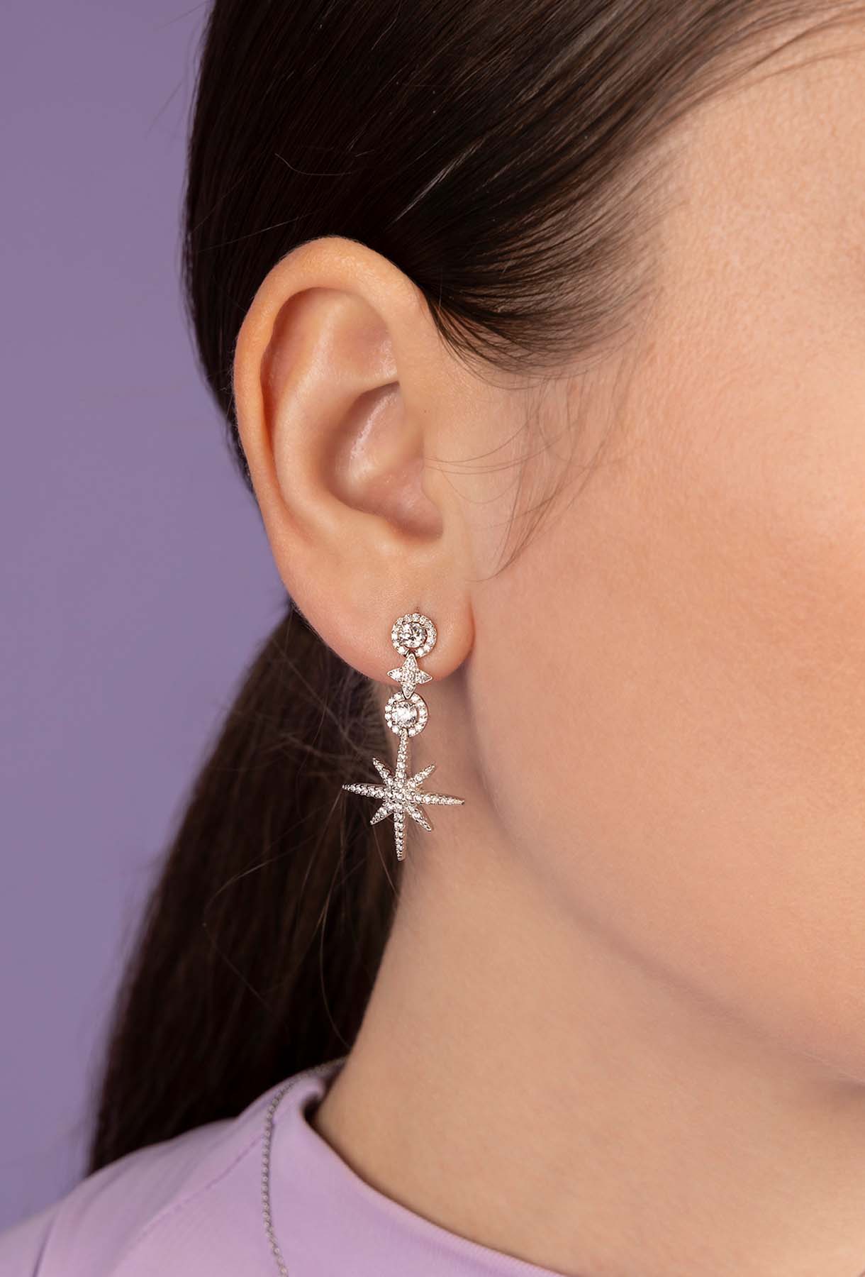Close-up of a person wearing a silver star-shaped earring with a purple background