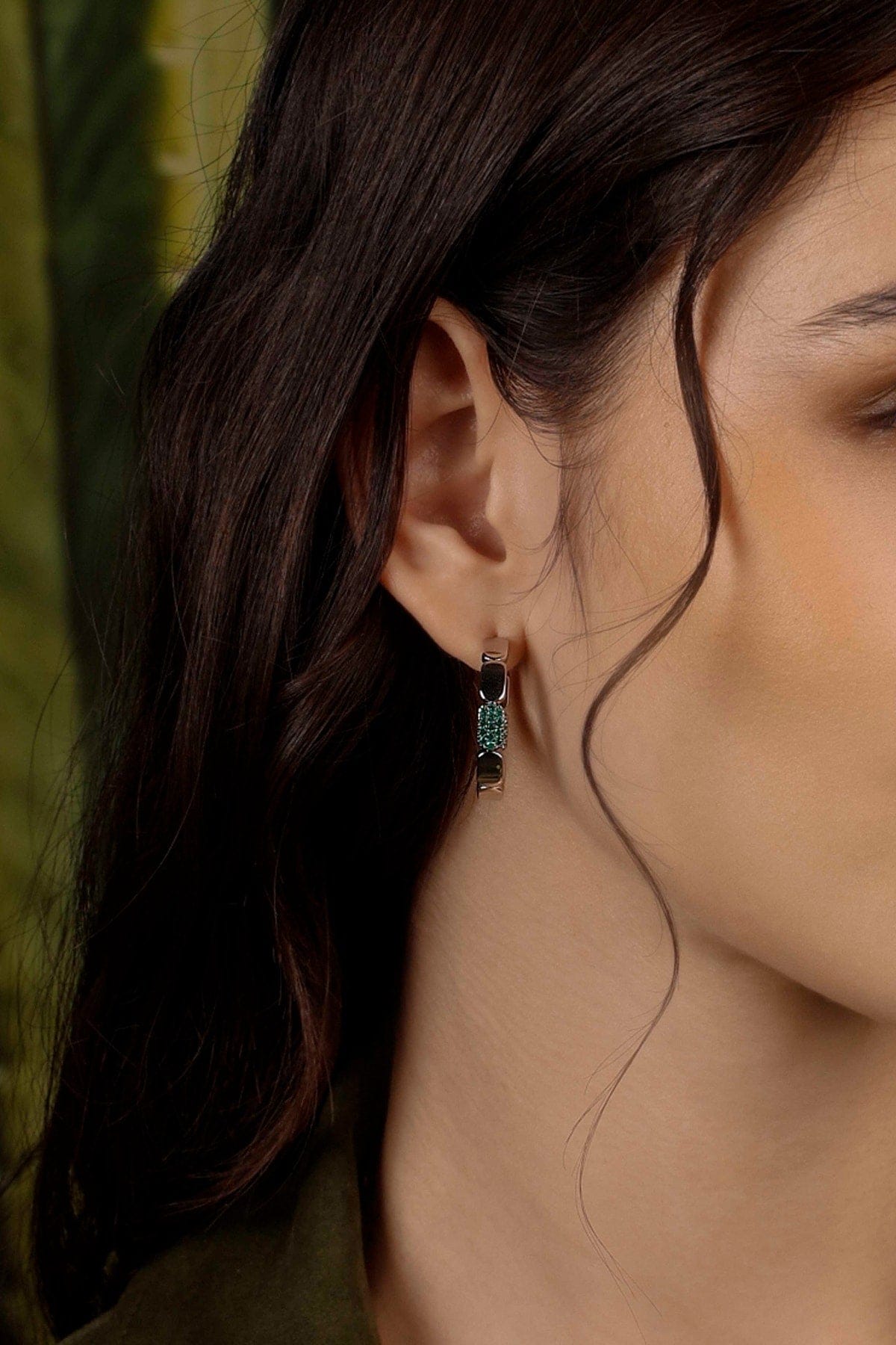 Close-up of a model wearing a silver earring with a green background