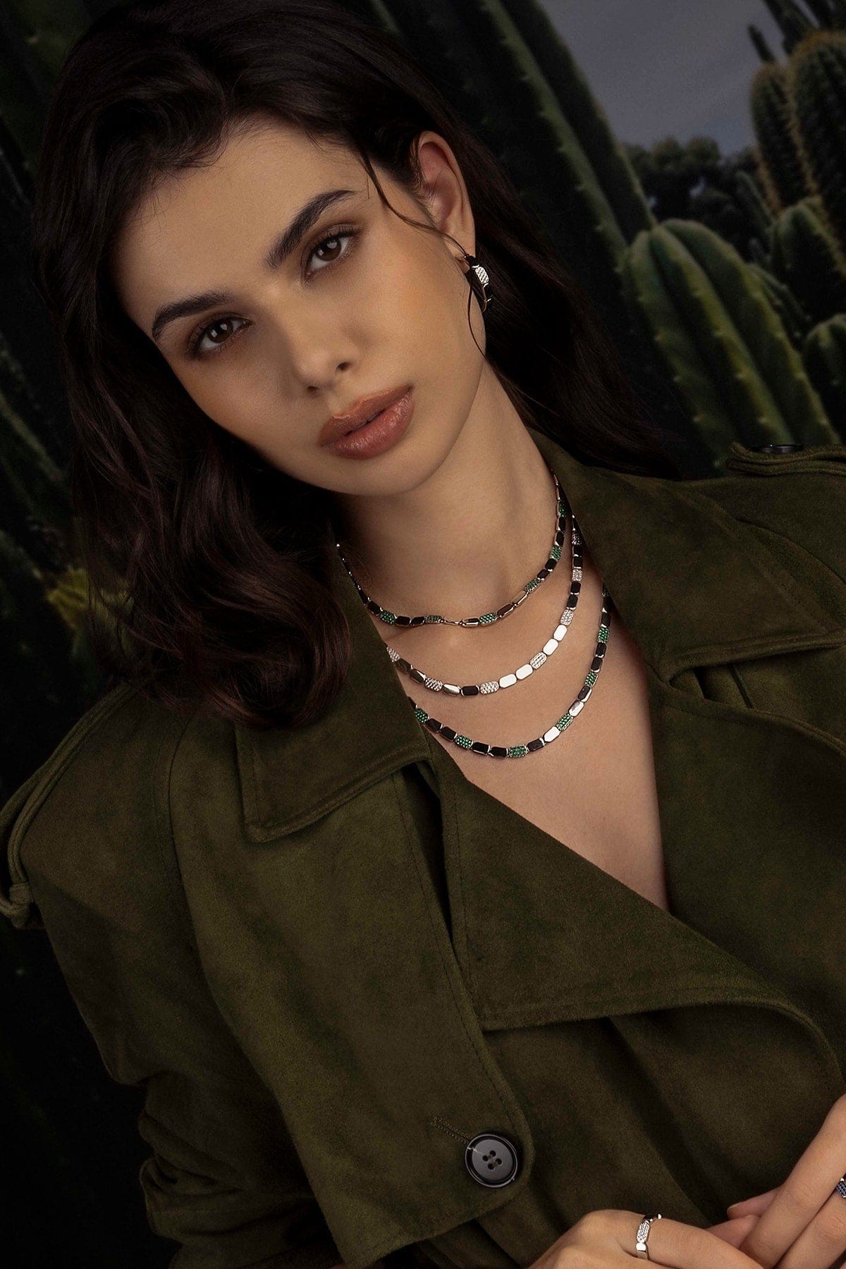 Woman wearing a green jacket and layered necklaces with cacti in the background