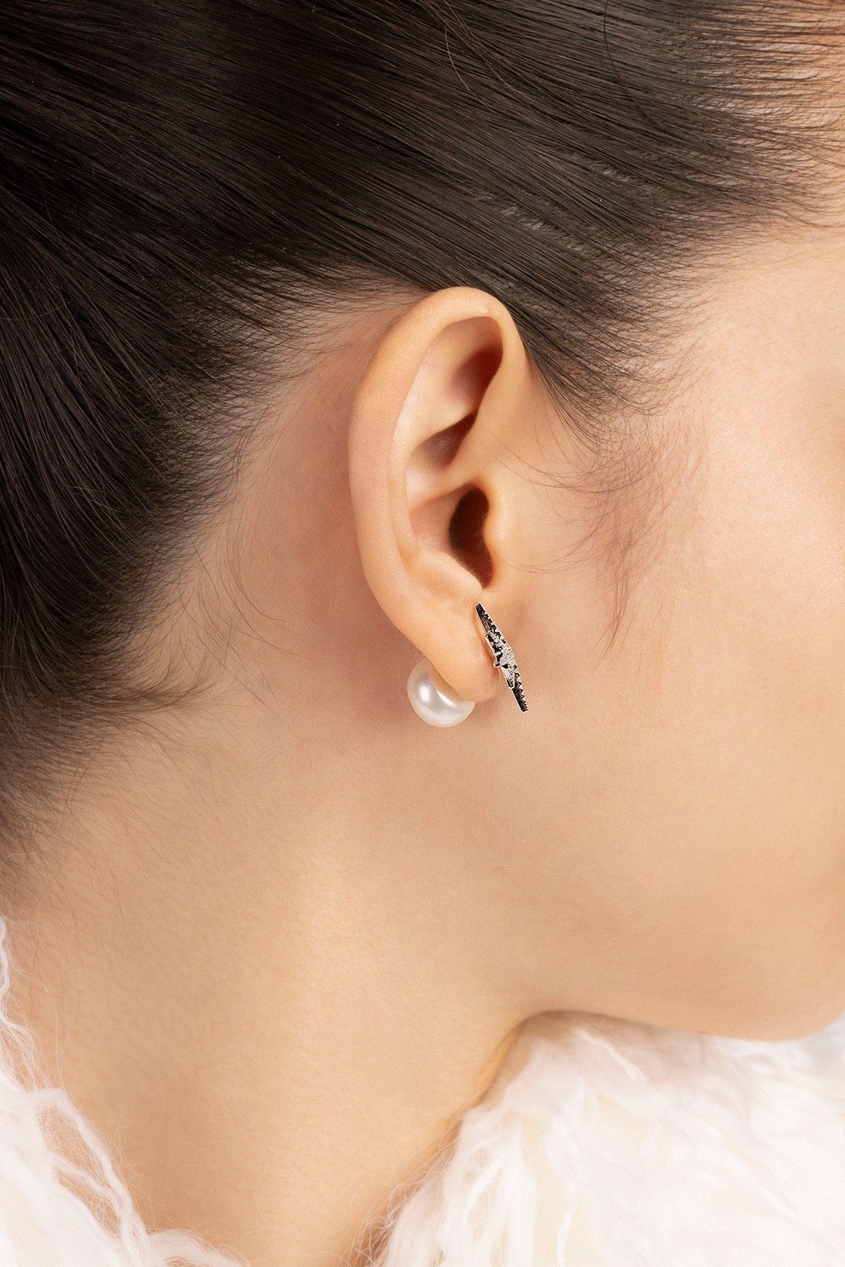 Close-up of an ear wearing a pearl earring with a star stud.
