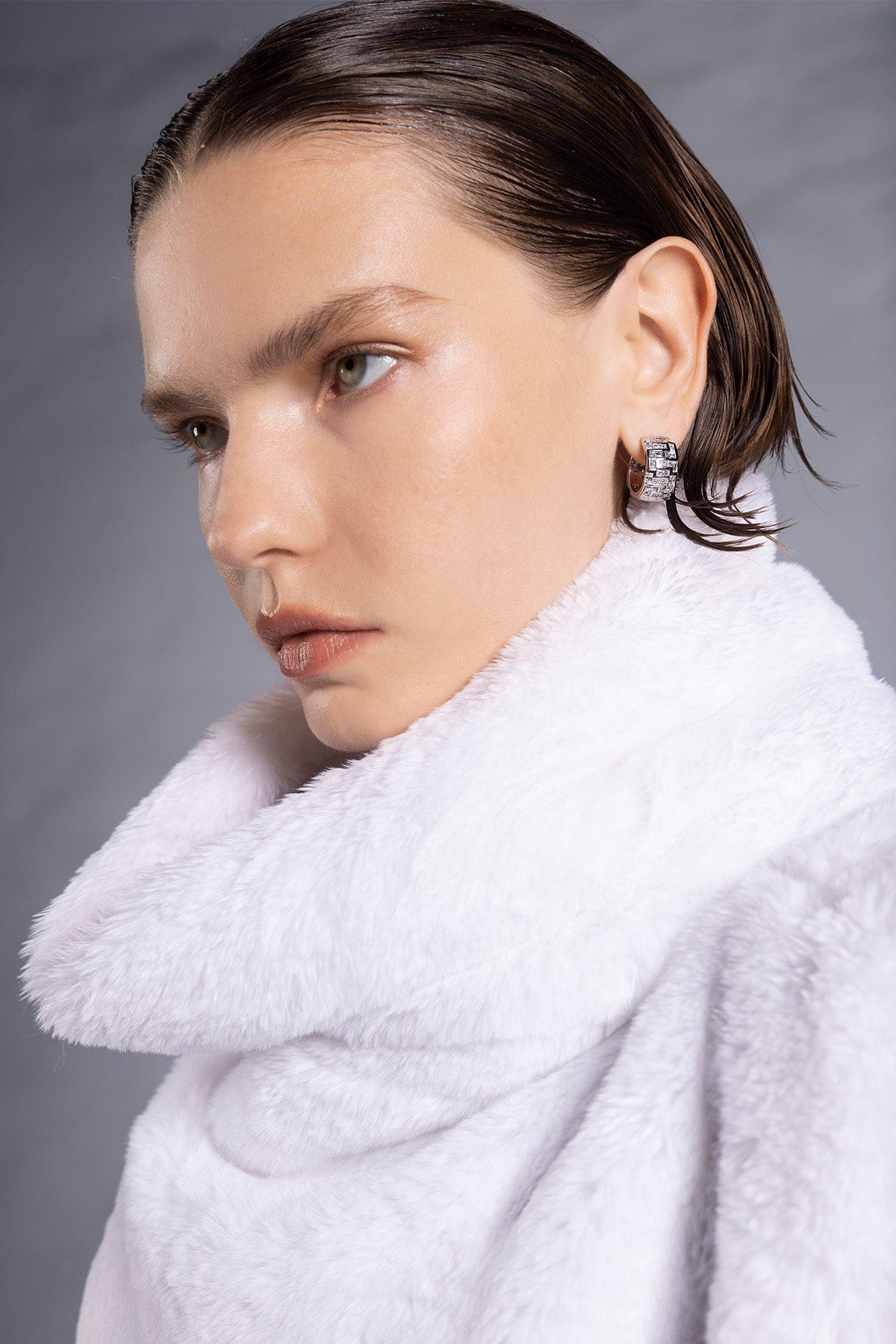 Woman wearing a white robe with APM MONACO labyrinth hoop earring in silver