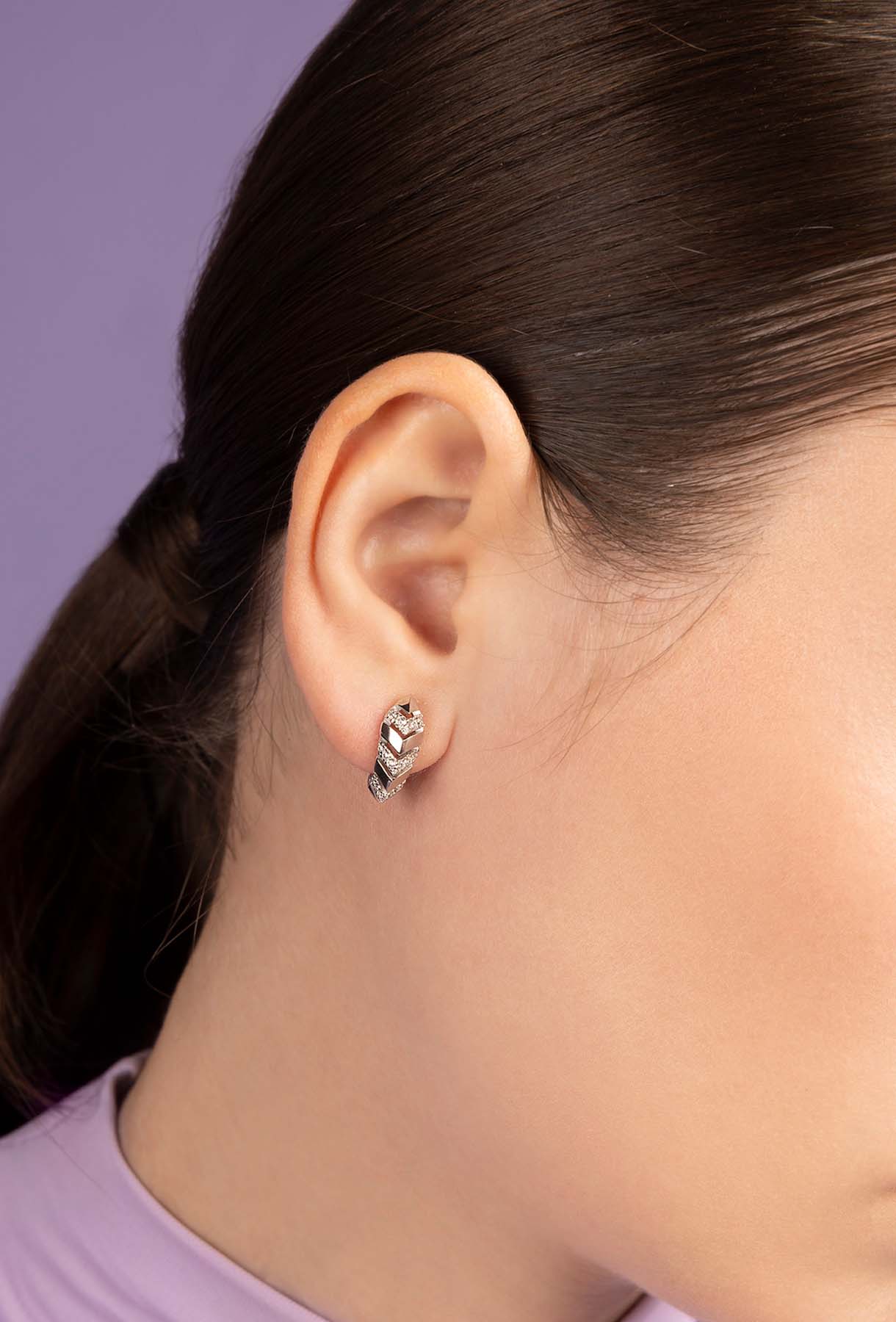 Close-up of a person wearing APM MONACO Silver-tone earring with a black design on a light purple background