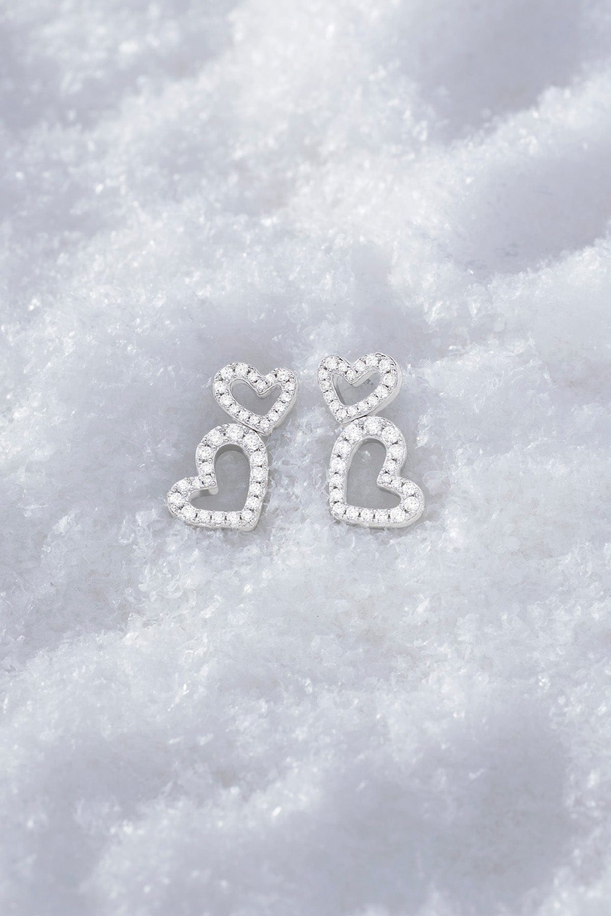 APM MONACO heart earrings in silver on soft snowy surface