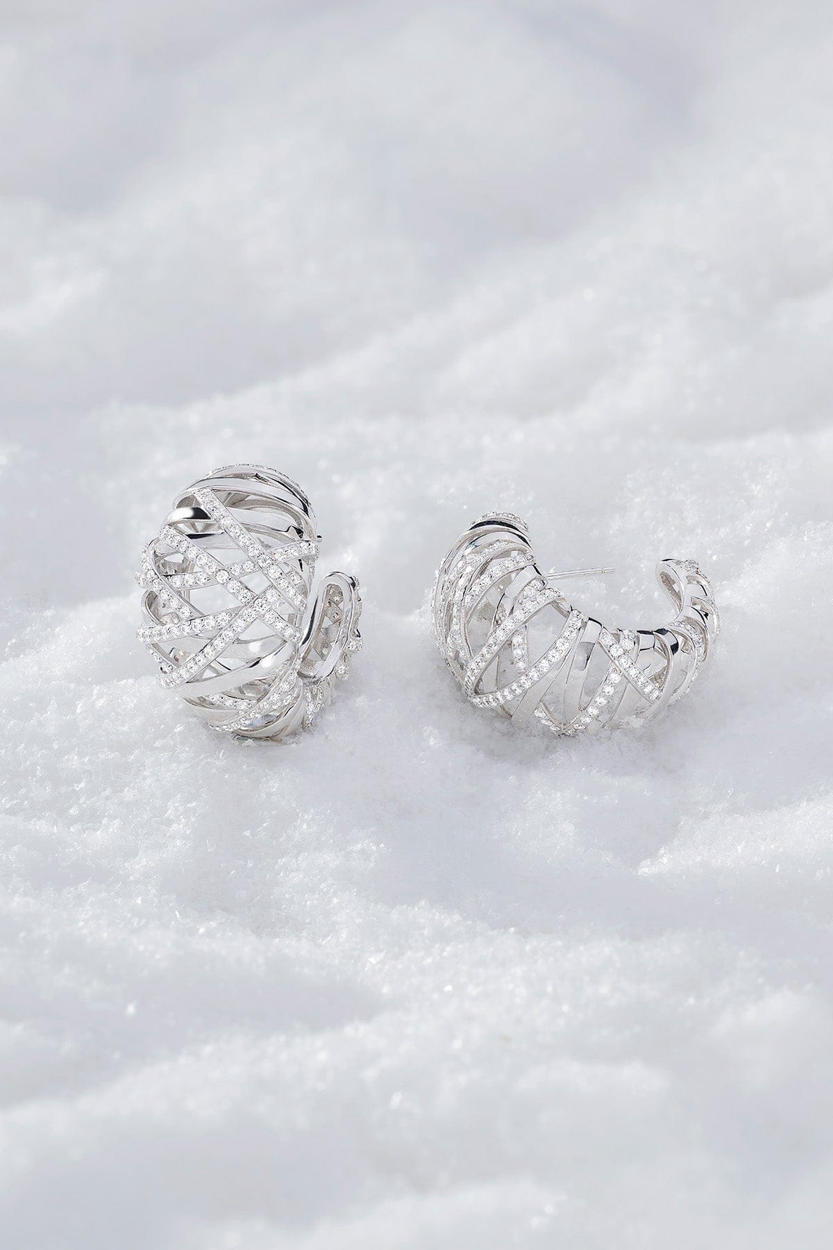 Pair of APM MONACO enlace hoop earrings in silver on a textured white surface