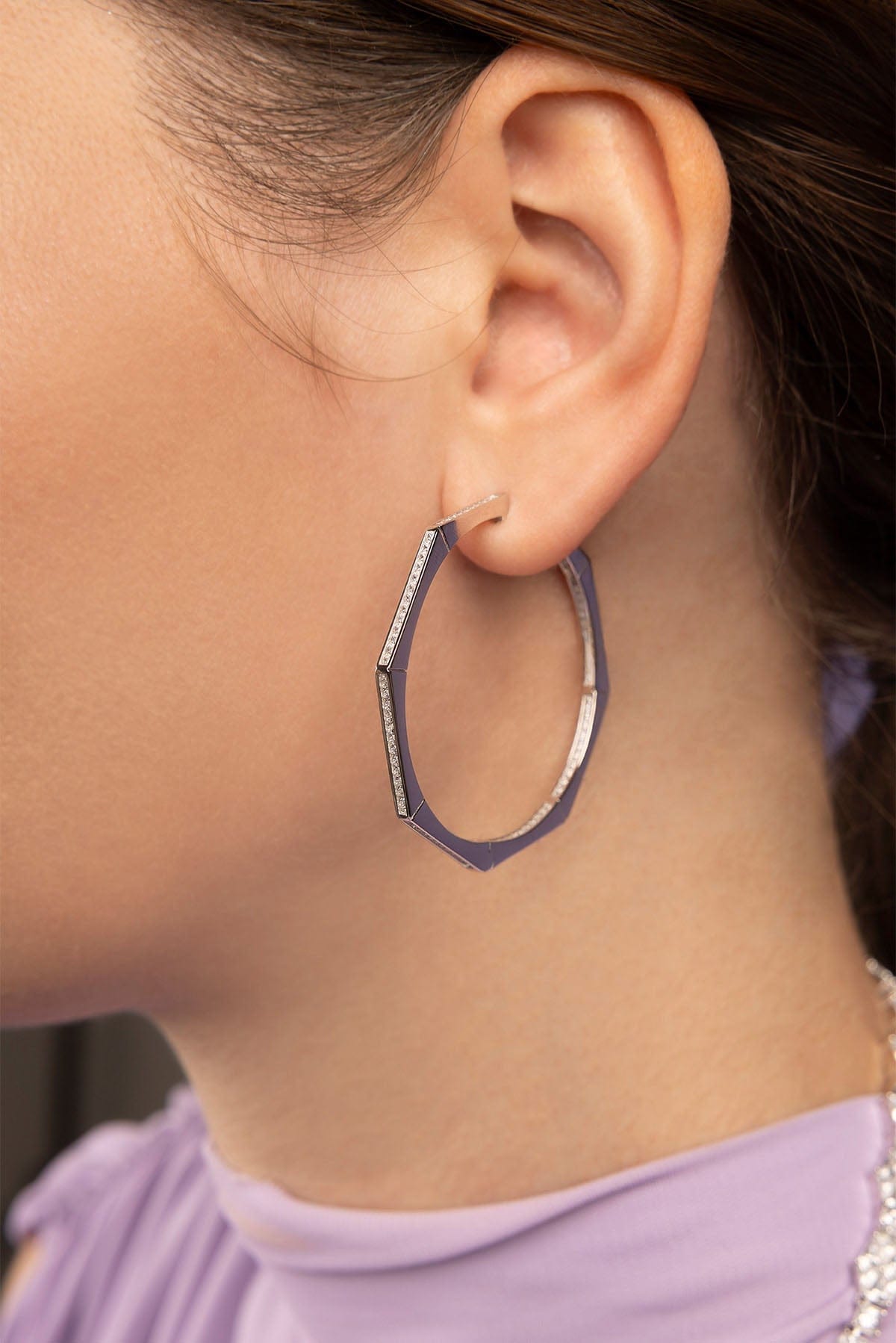 Close-up of an ear wearing a silver hoop earring with a purple background