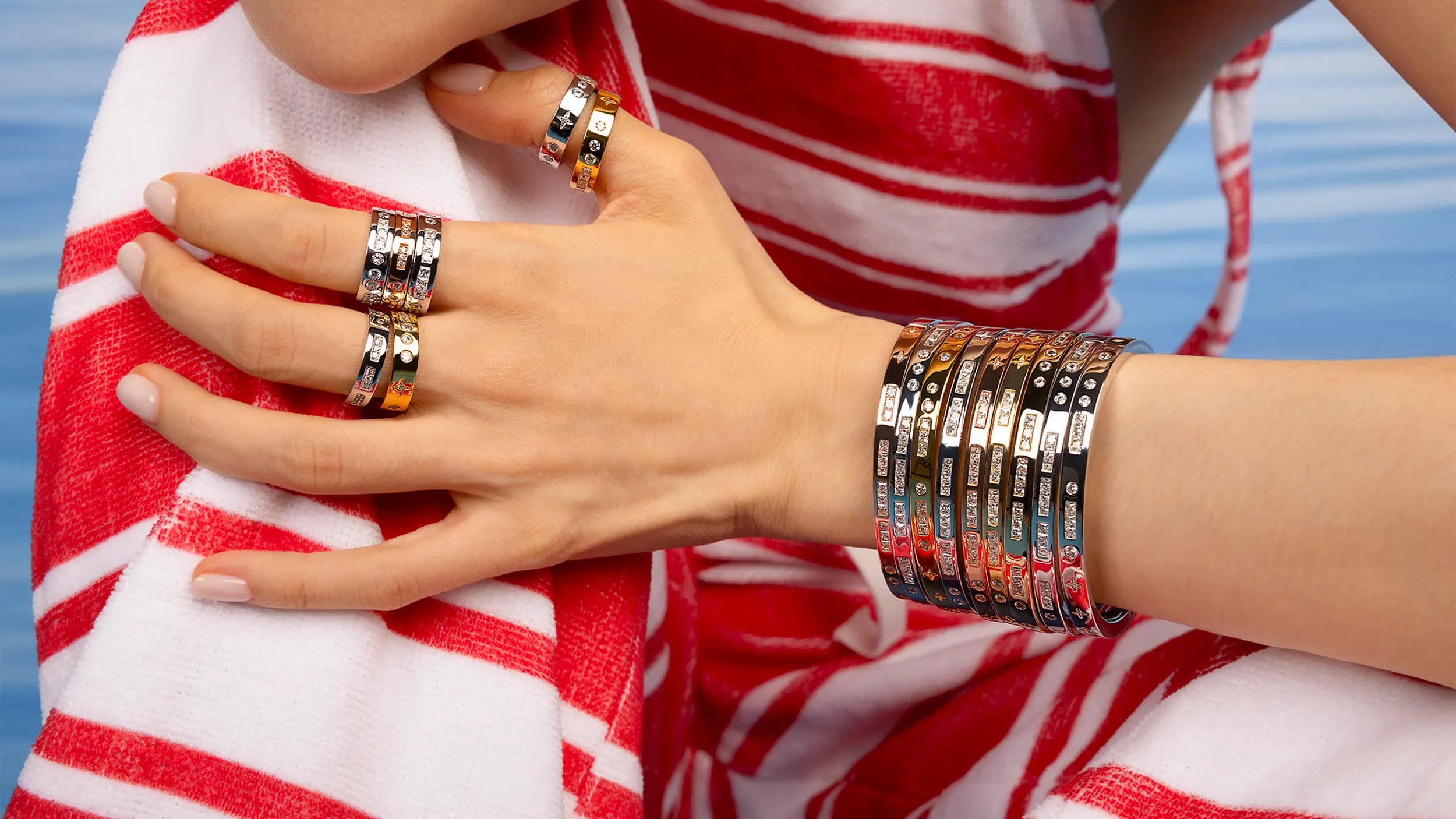 Hand wearing multiple APM MONACO morse code bracelets and rings on a red and white striped fabric background