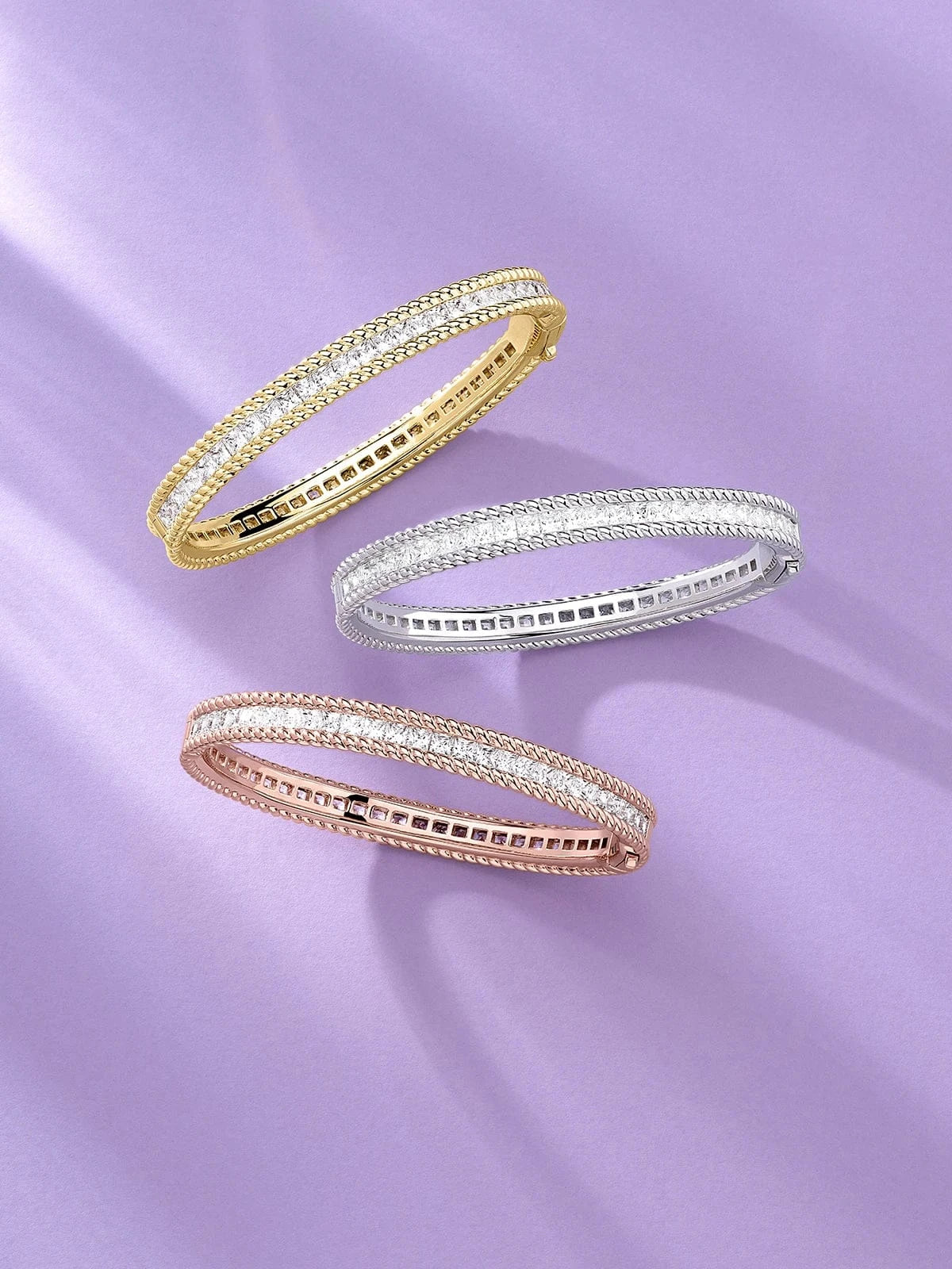 APM Monaco Torsade bracelets gold, silver, and rose gold bracelets on a purple fabric background