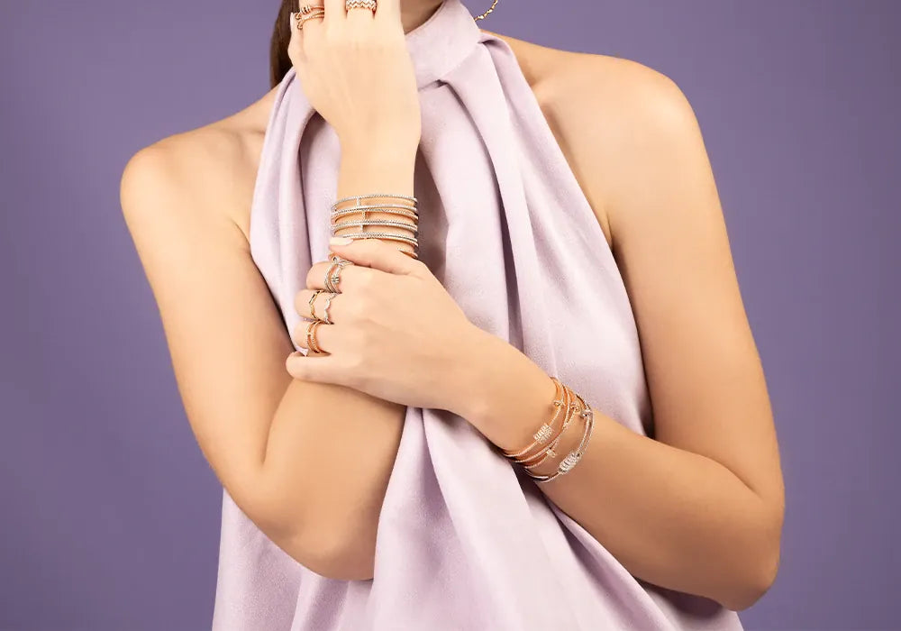 Woman wearing APM Monaco Croisette jewelry including rings, bracelets, and a necklace on a purple background