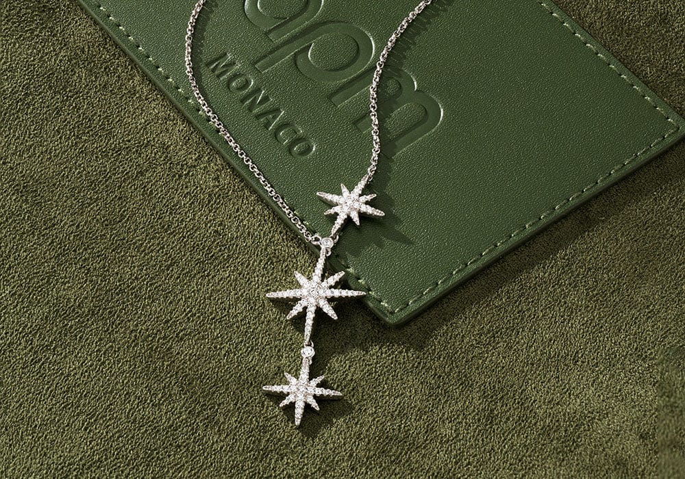 Silver star-shaped necklace on a green leather surface with 'APM MONACO'