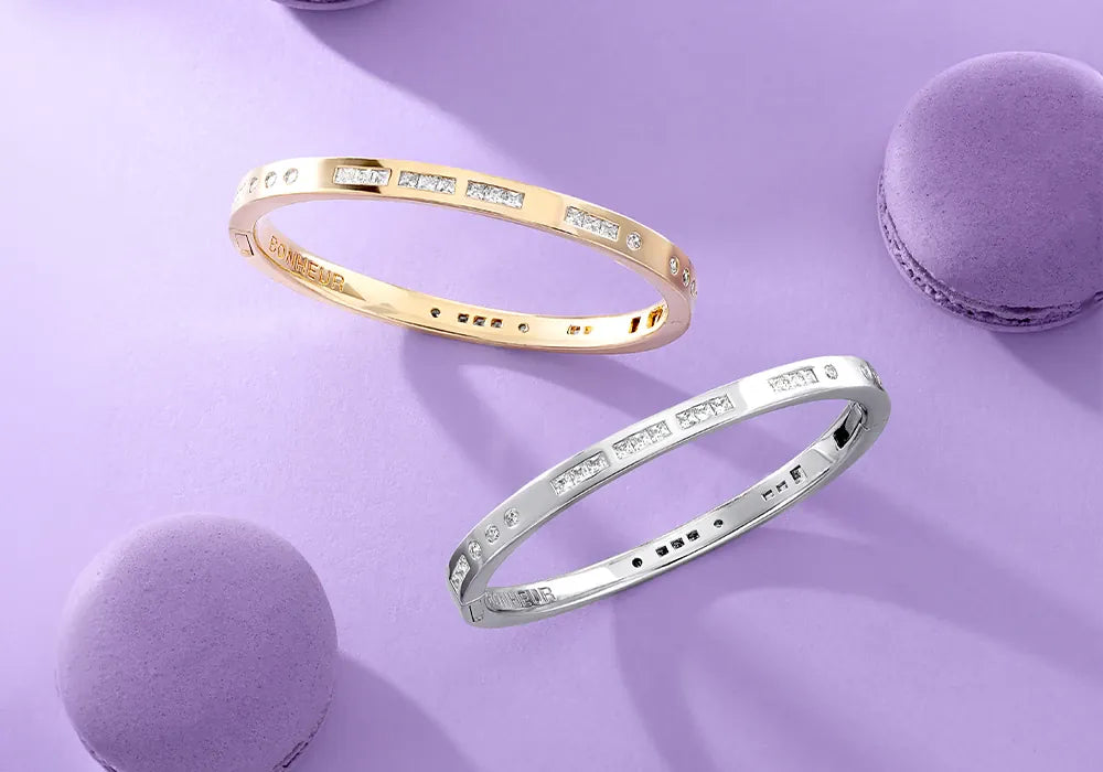APM Monaco gold and silver Morse Code bracelets on a purple surface with macarons.