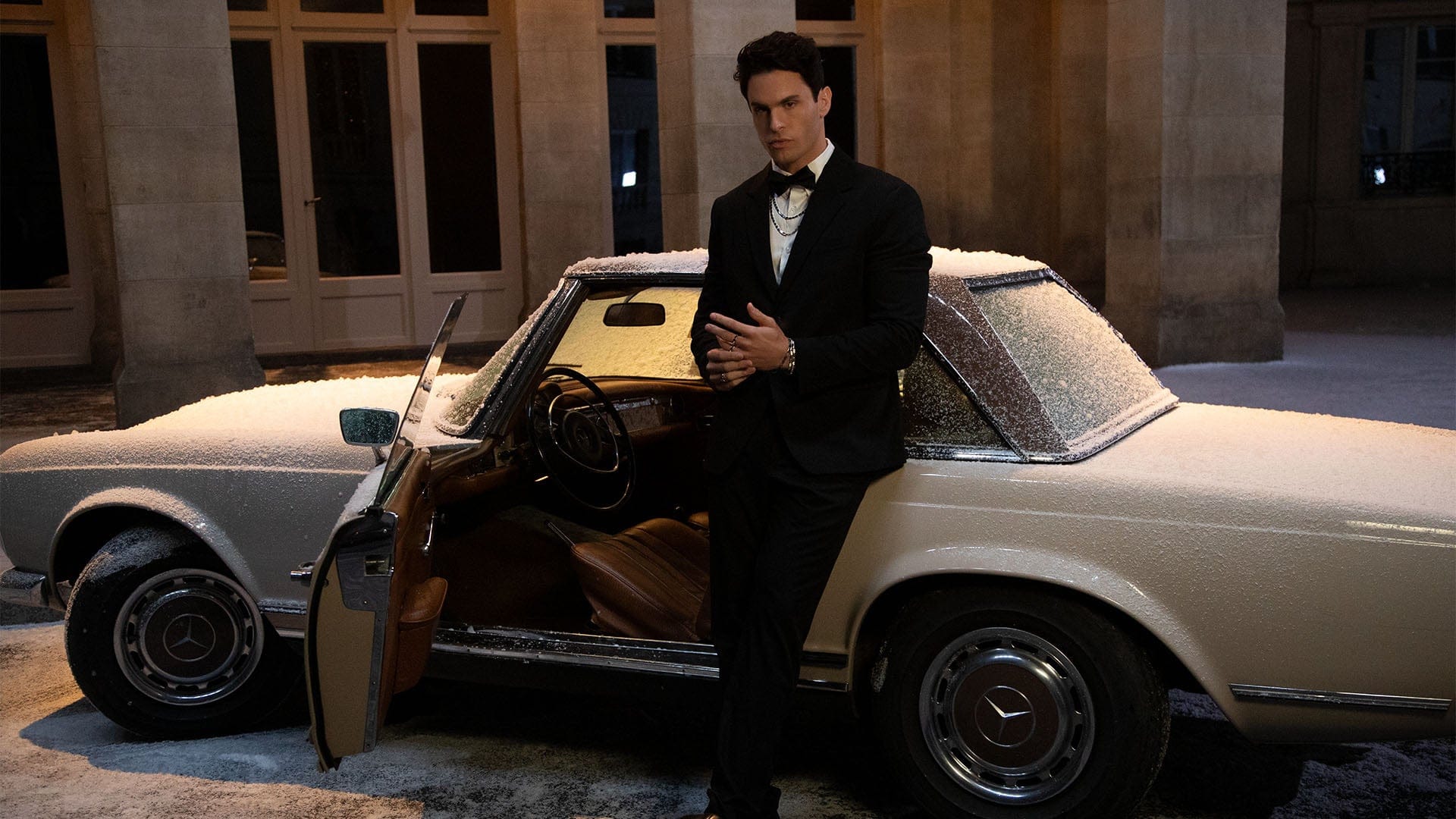 Man in a tuxedo standing next to a vintage car with APM MONACO ice jewelry set