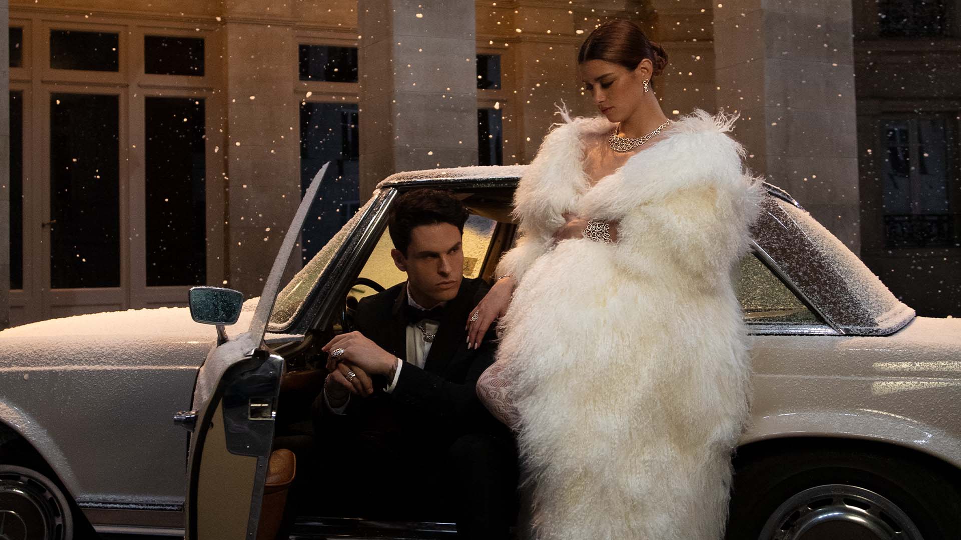 Man opening a car door for a woman with APM MONACO heart jewelry set in a white at night.