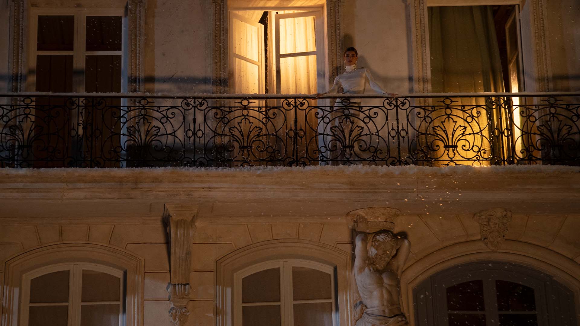 Person with APM MONACO hiver jewelry set standing on a balcony of an elegant building at night.