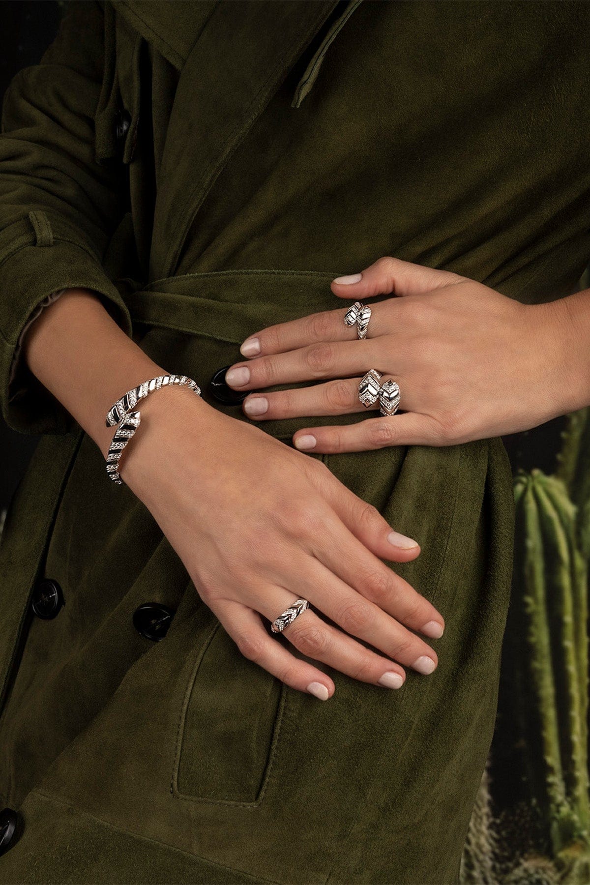 Close-up of hands wearing multiple apm monaco rings on a green coat background