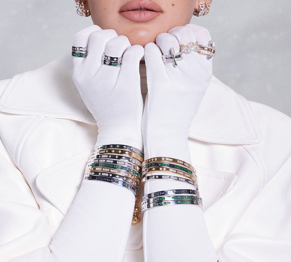 Close-up of a person wearing multiple morse code bracelets and rings on a white background
