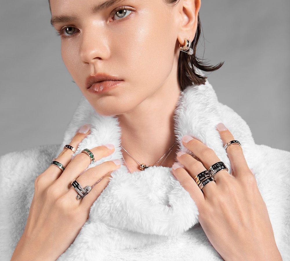 Woman wearing multiple APM MONACO morse code rings on fingers and earrings, with a neutral background