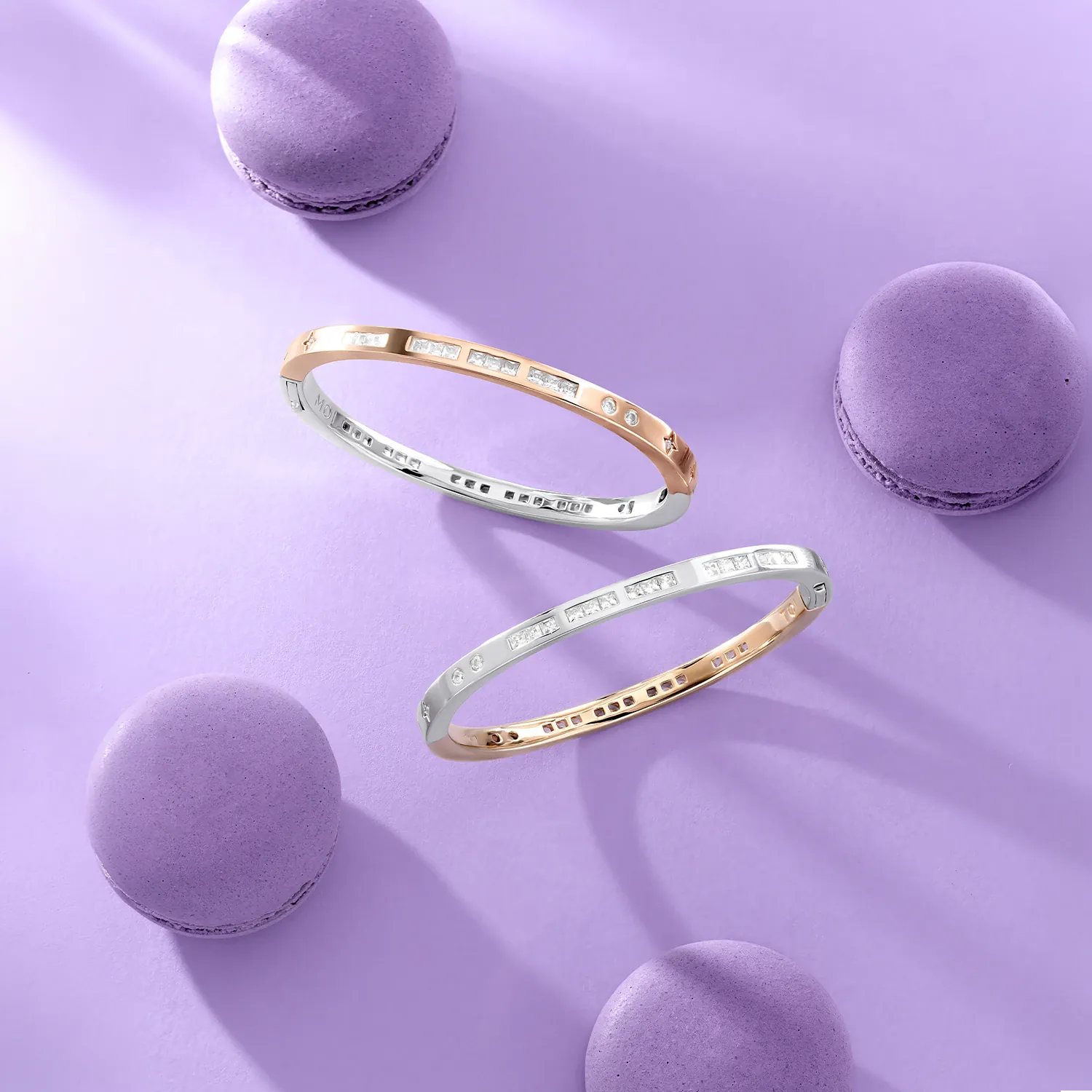 Two Rose gold APM Monaco Morse Code bracelets on a purple surface with macaron cookies.