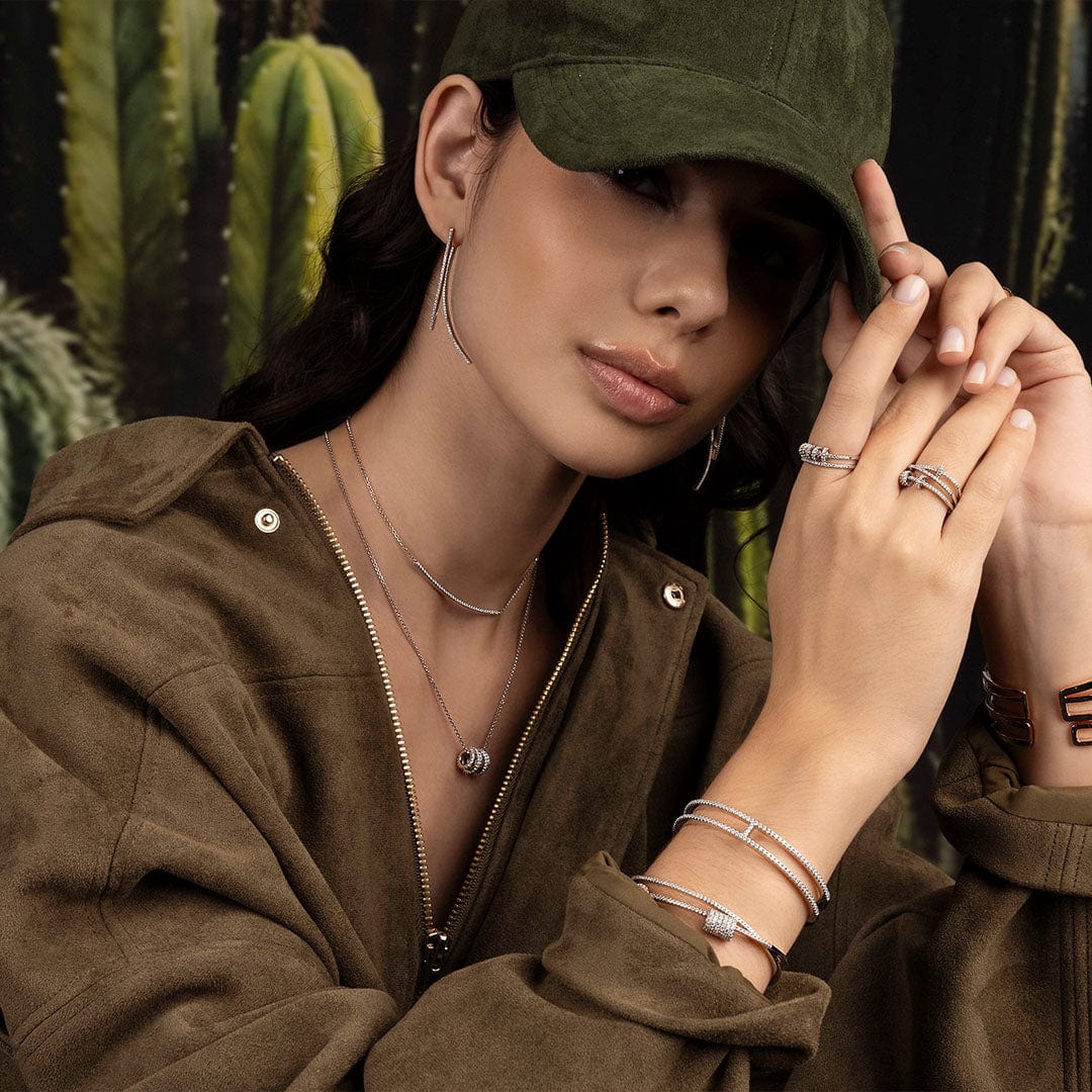 Woman wearing a green cap and brown jacket with APM MONACO must-have jewelry, cactus plants in the background