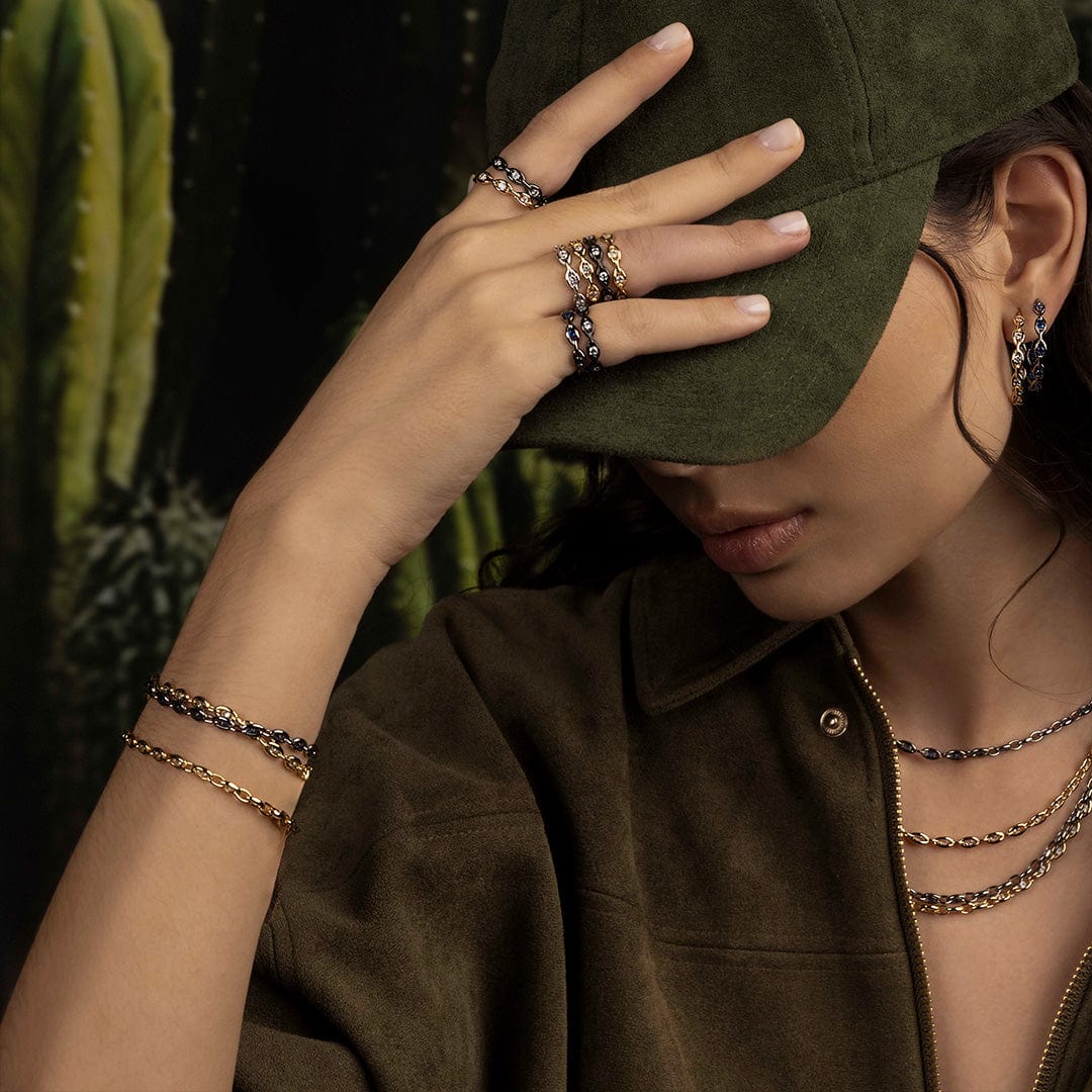 Person wearing a green cap and multiple pieces of jewelry with a cactus in the background