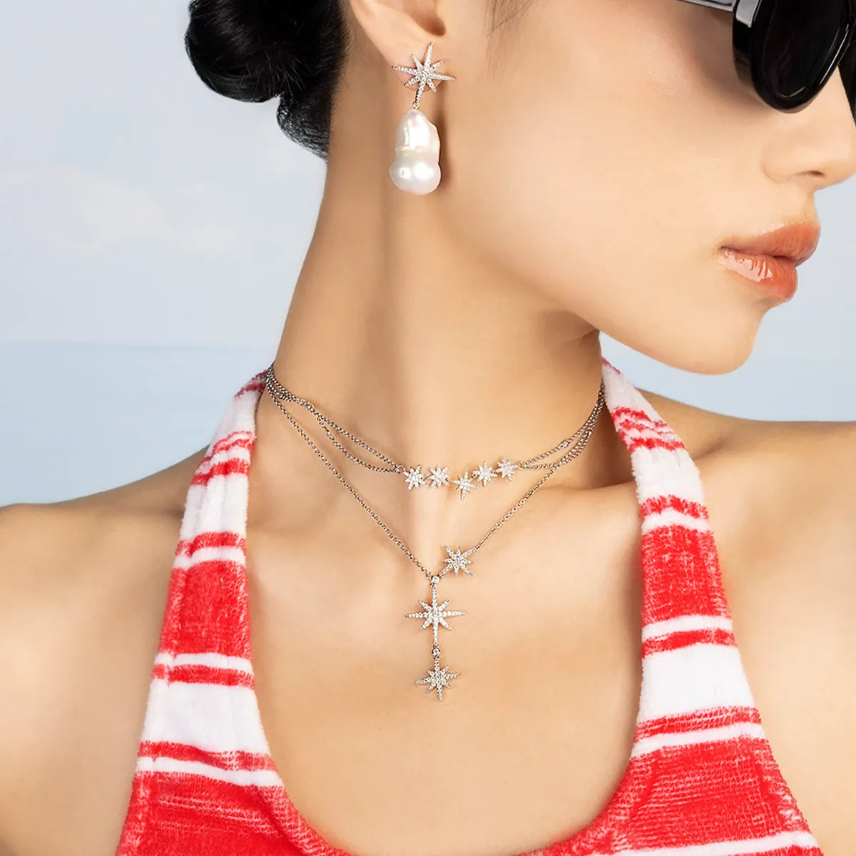 Woman wearing APM MONACO Meteorites necklace and earrings with a red and white striped top against a light blue background