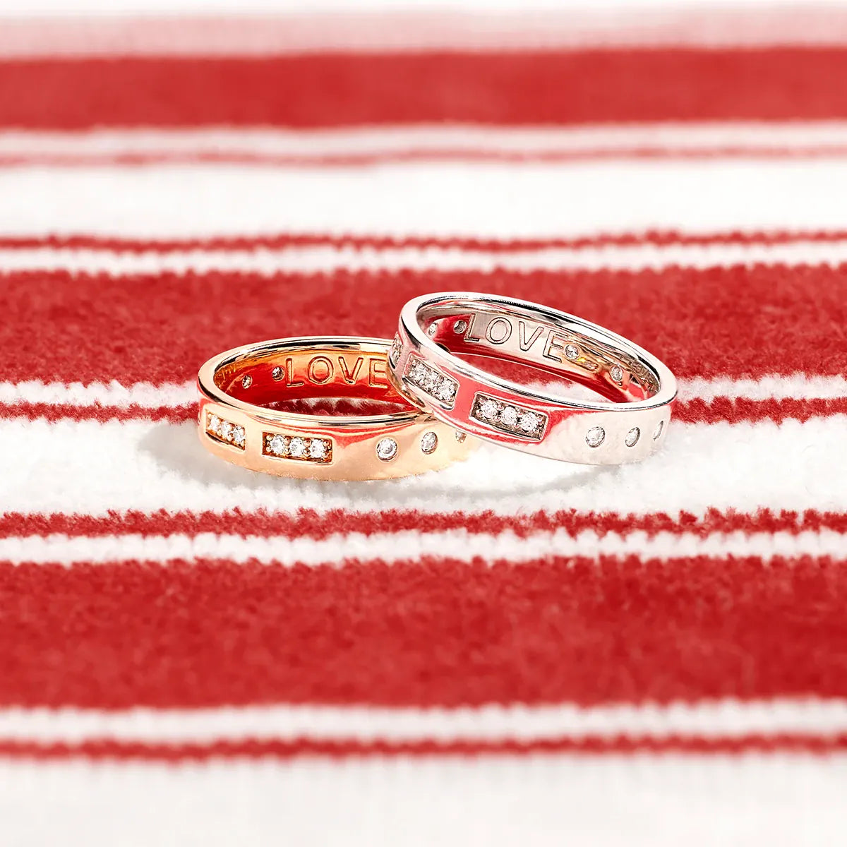 Two APM MONACO rose and yellow rings with 'LOVE' engraving on a red and white striped background
