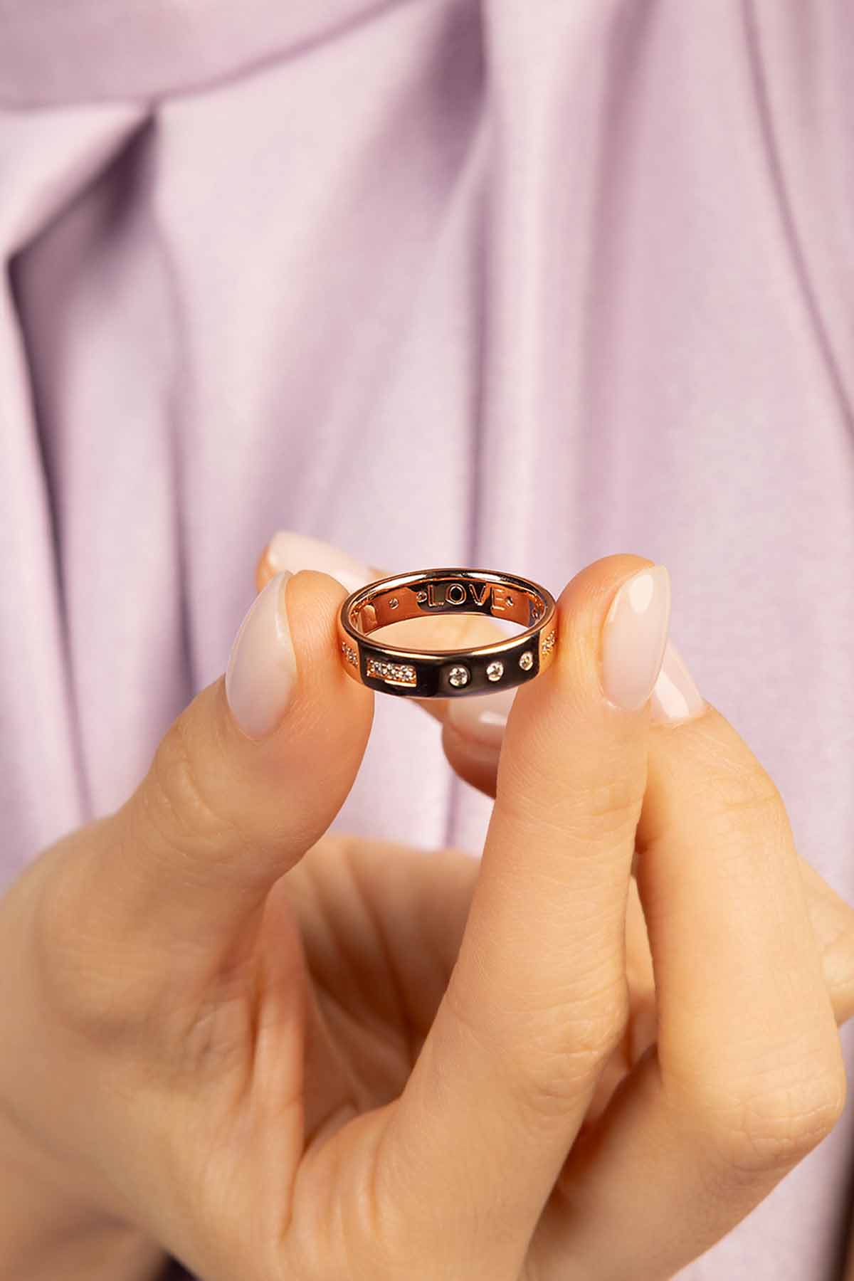 Hand holding a rose gold ring with small stones against a light purple fabric background