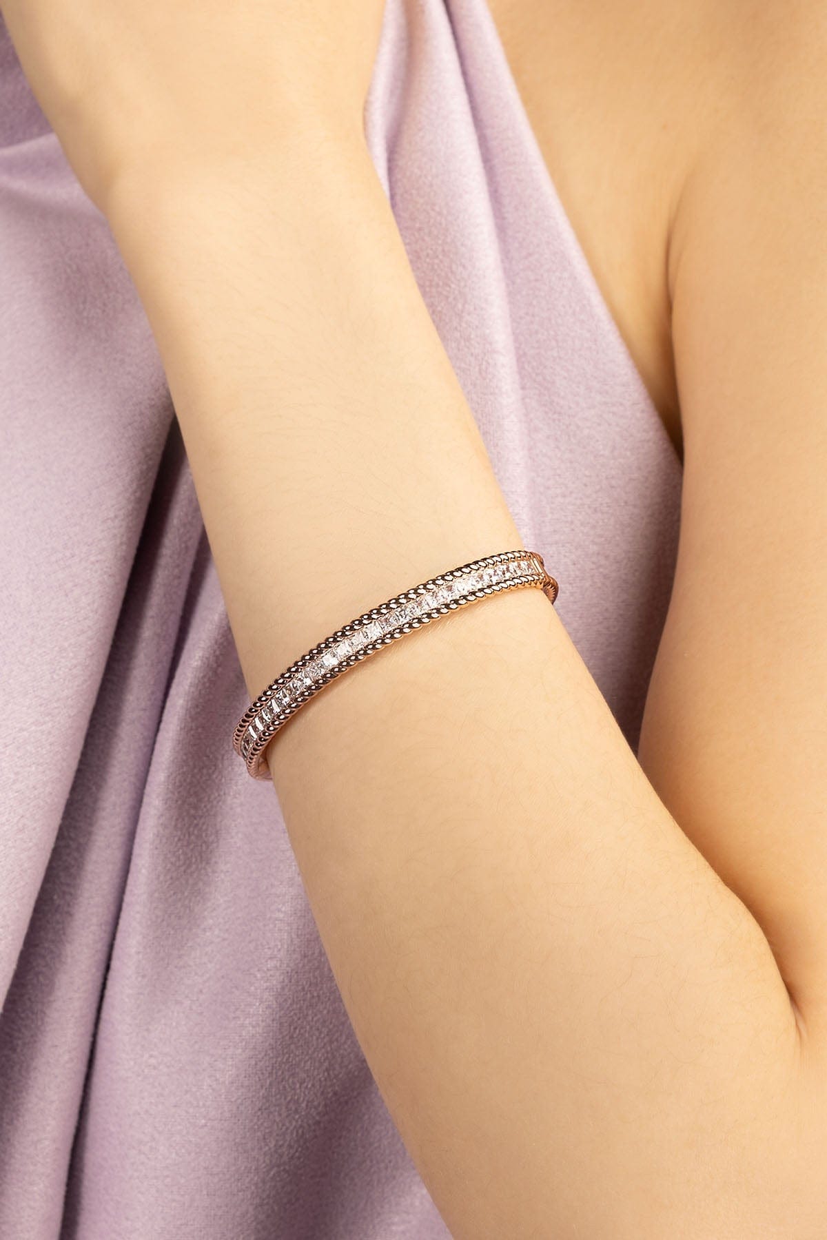 Rose gold bracelet on a person's wrist with a soft pink fabric background