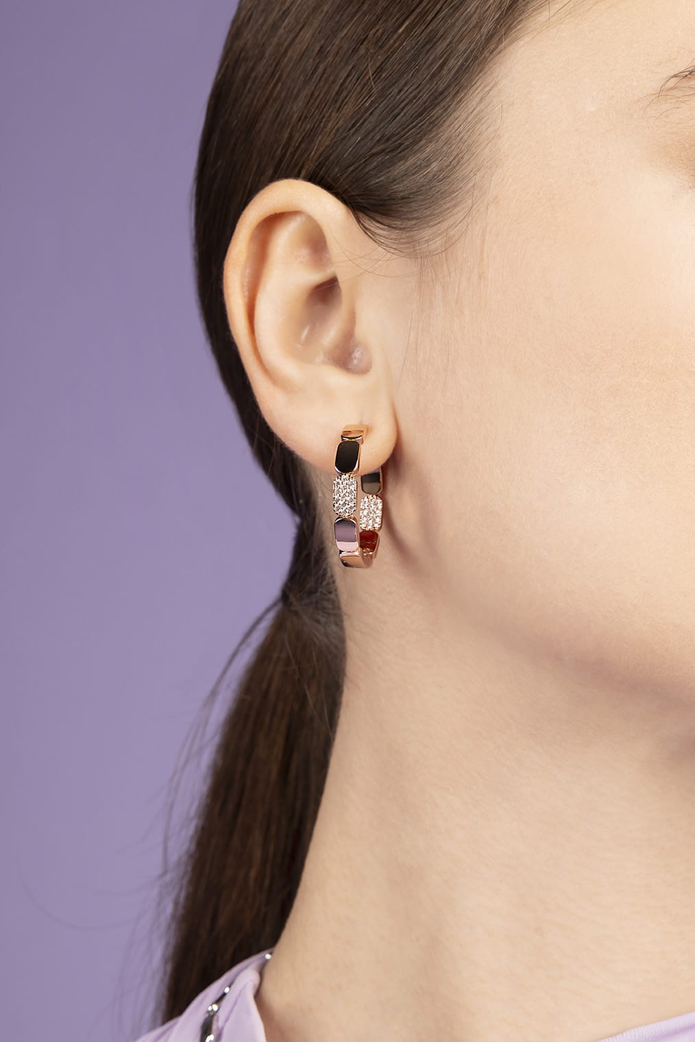 Close-up of a person wearing a pair of hoop earrings with a purple background