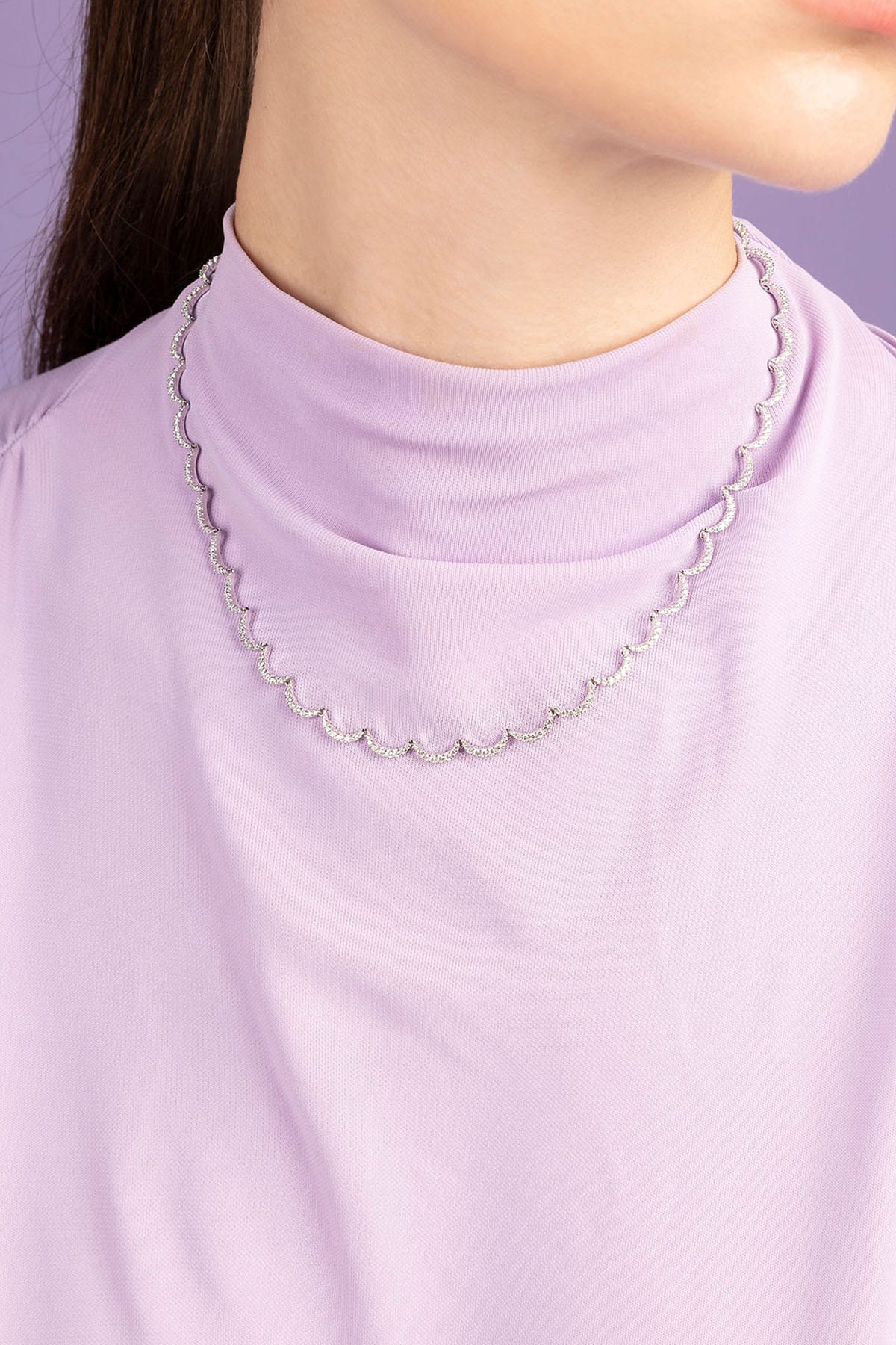 Person wearing APM MONACO white wavy chain necklace against a light purple background