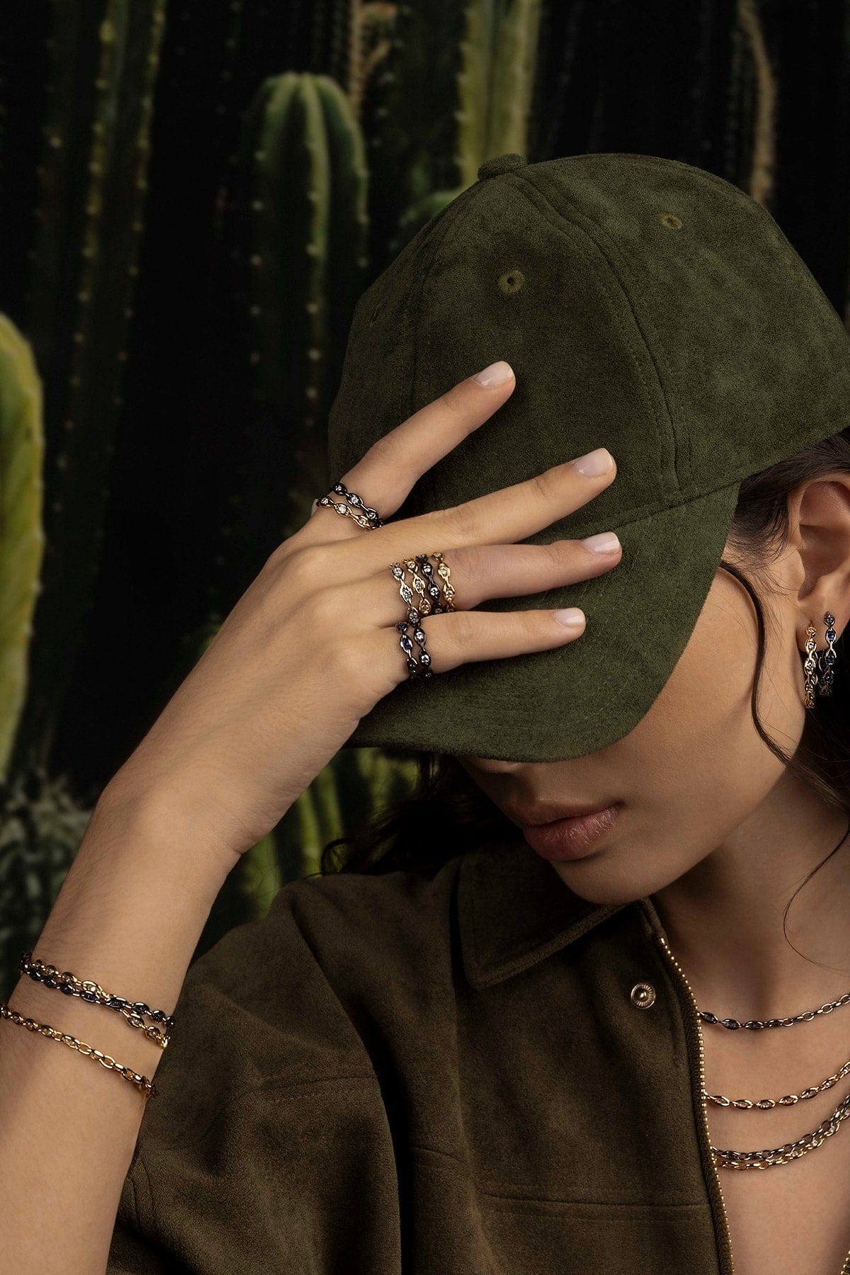 Person wearing a green cap and multiple rings with cacti in the background