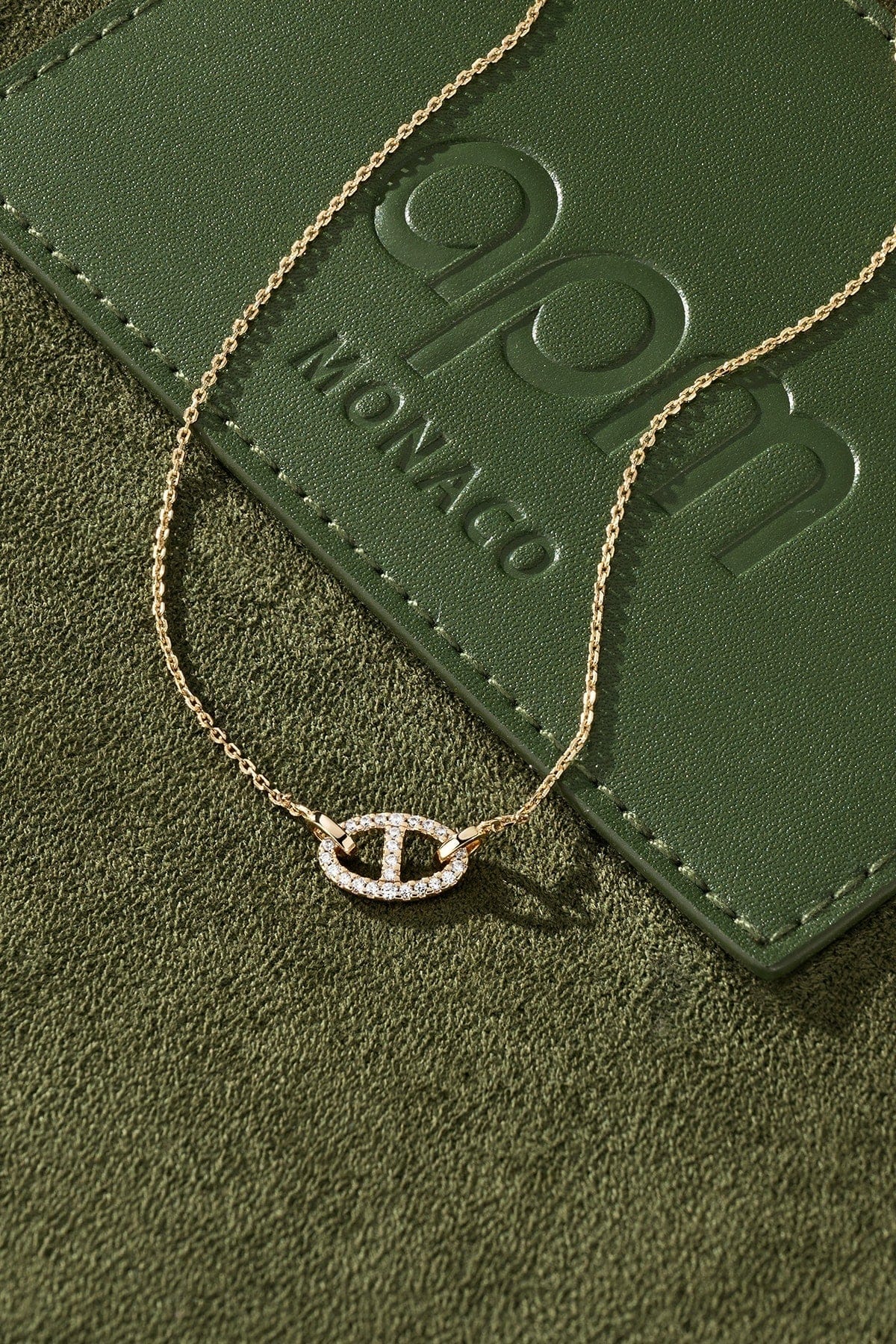 Gold necklace with a diamond pendant on a green textured surface