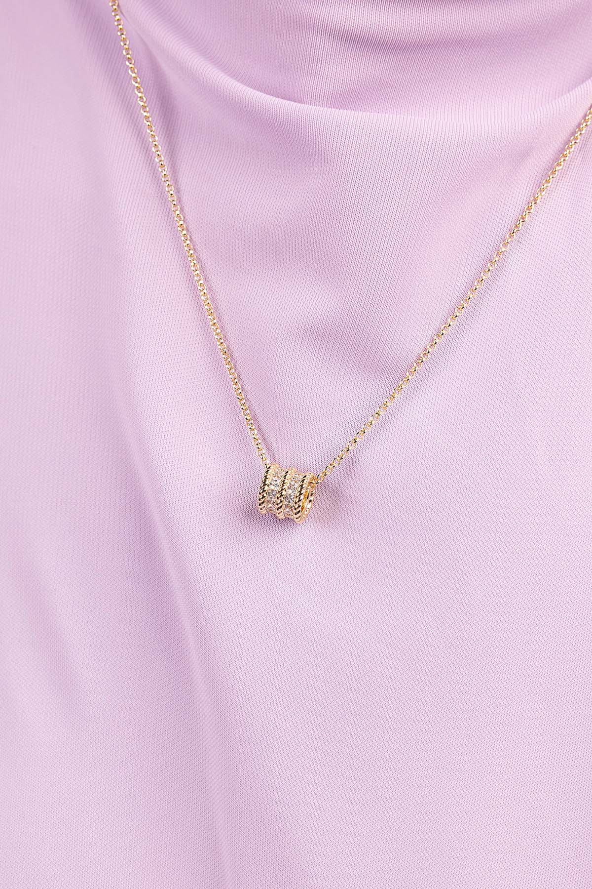 Gold necklace with a small pendant on a pink background