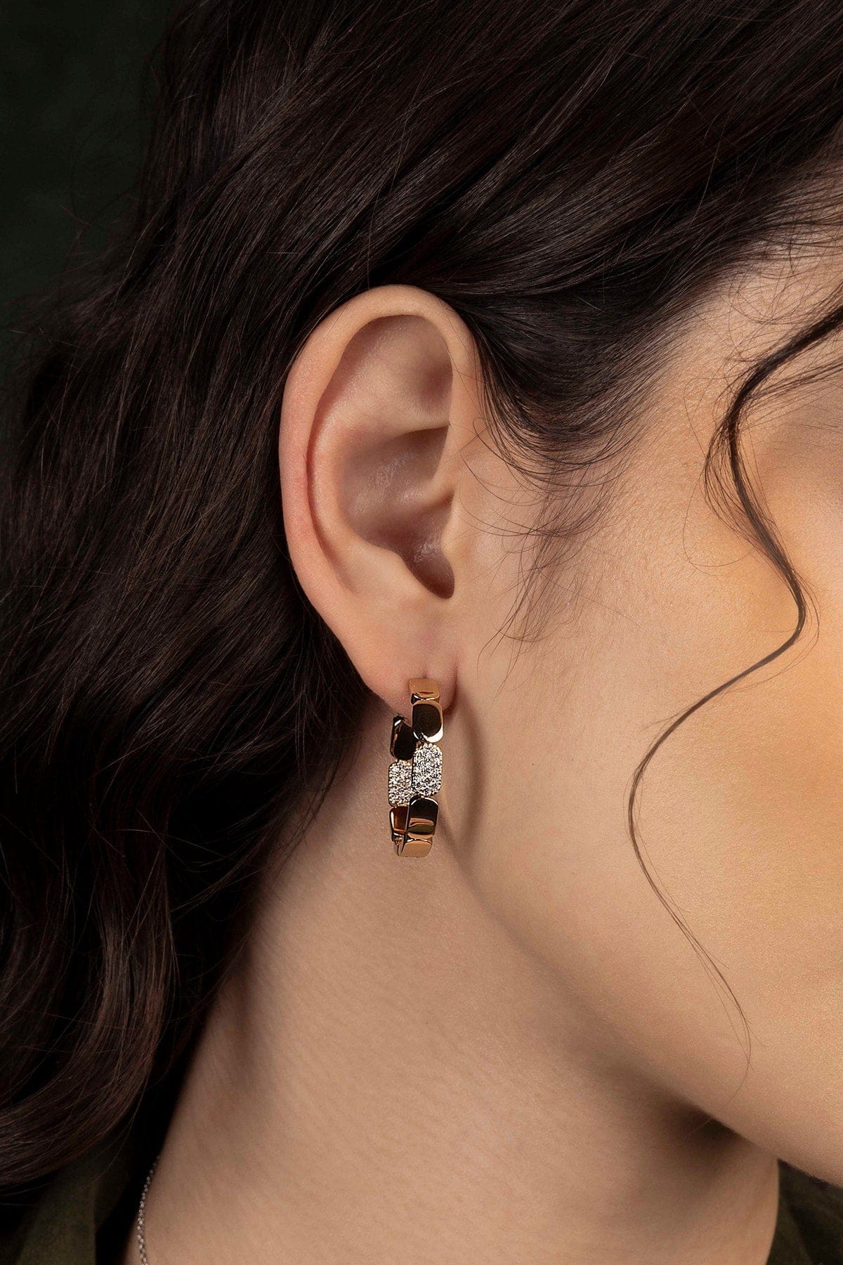 Close-up of an ear wearing a hoop earring with a dark background