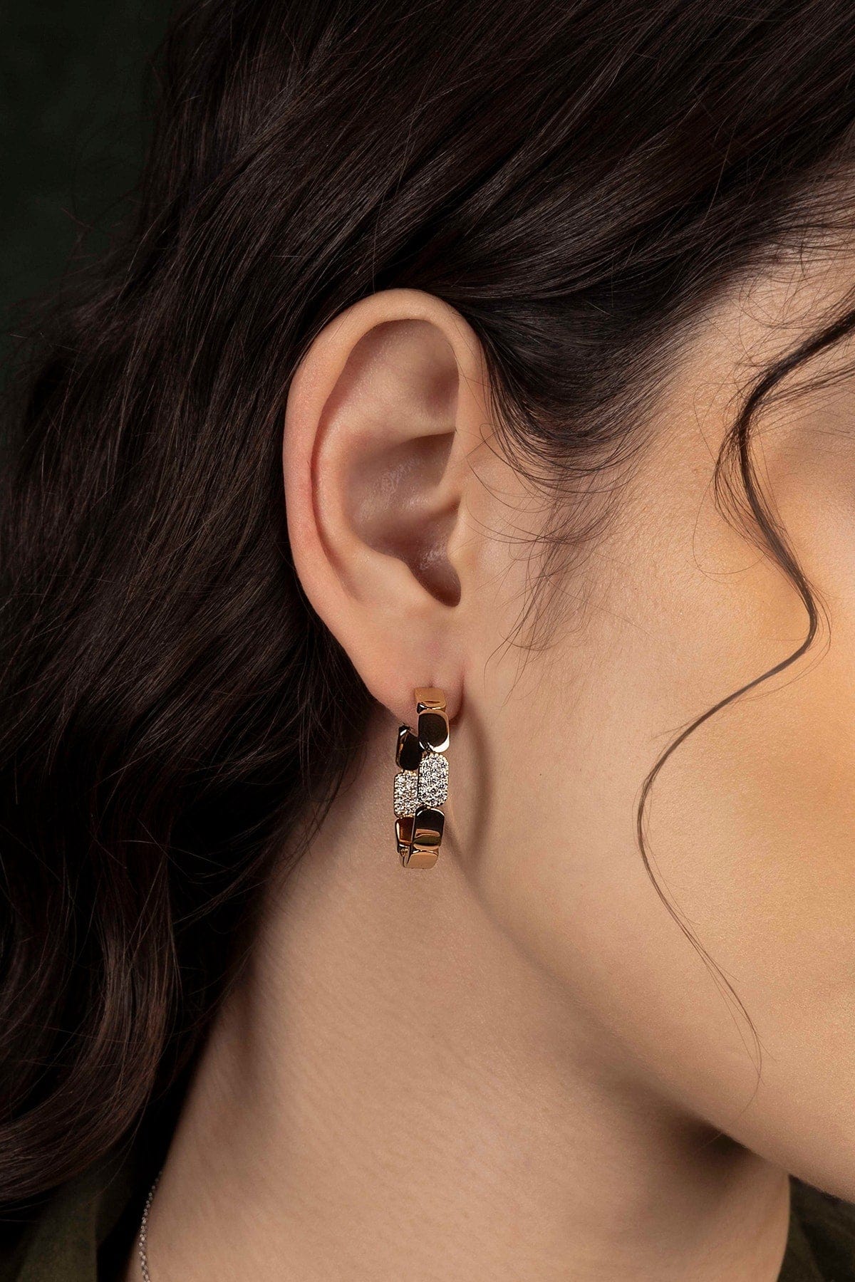 Close-up of an ear wearing a hoop earring with a dark background