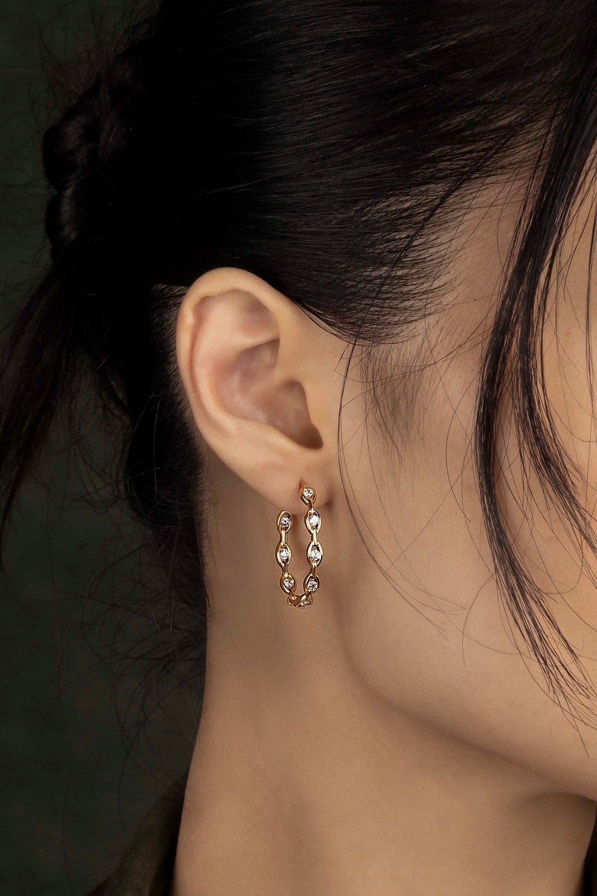 Close-up of an ear wearing a gold earring with a dark background