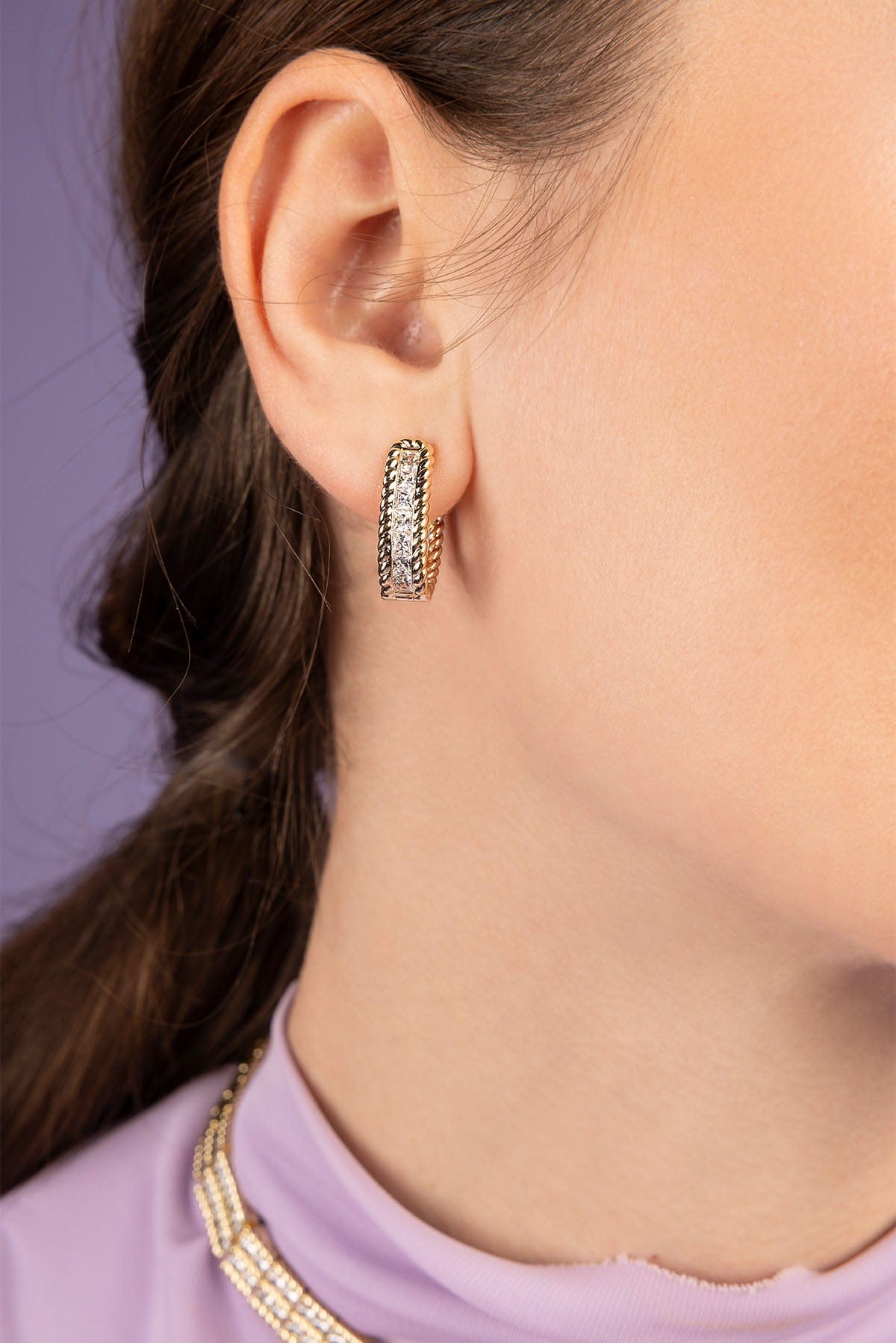 Close-up of a person wearing gold hoop earrings with a purple background