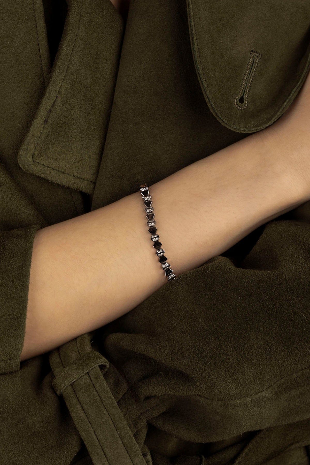 APM MONACO up and down bracelet in silver on a wrist with a dark khaki coat in the background