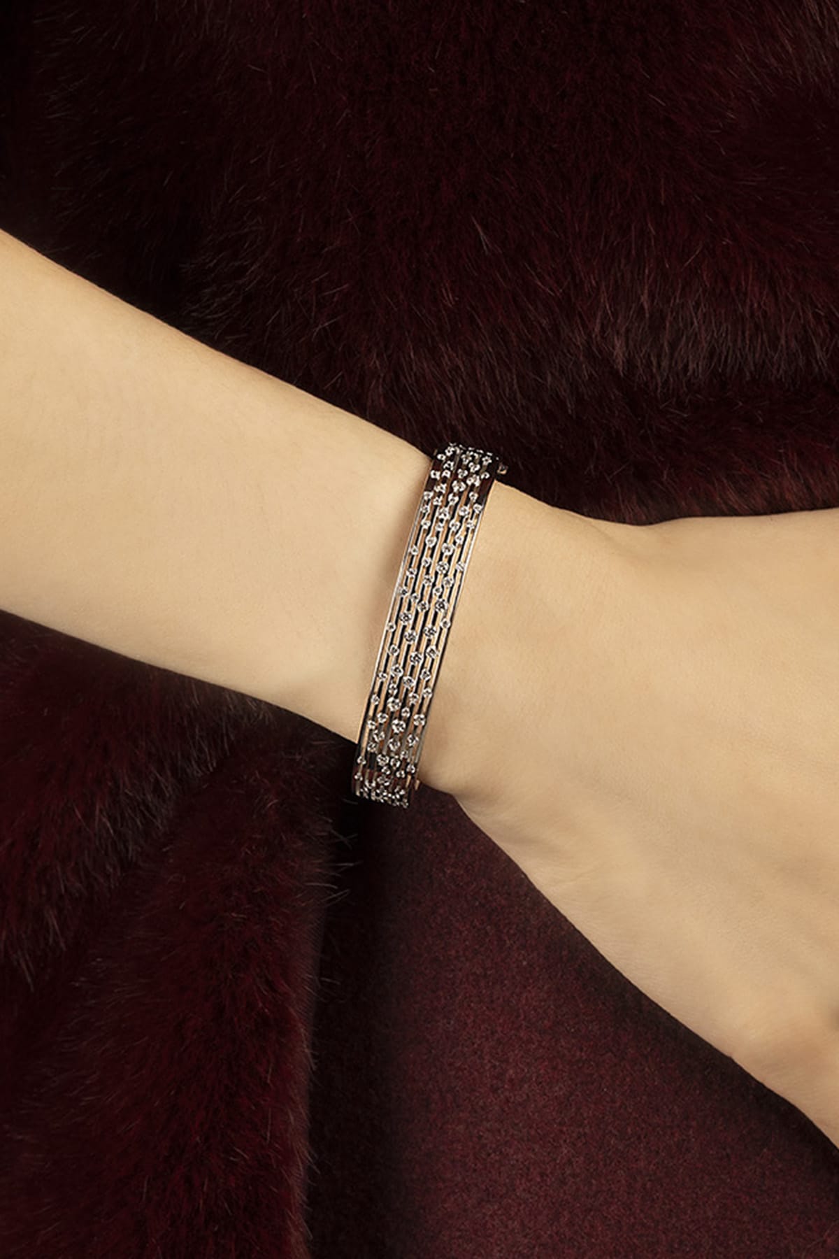 Woman wearing APM Monaco bracelet, layered shimmer against burgundy fur elegance.