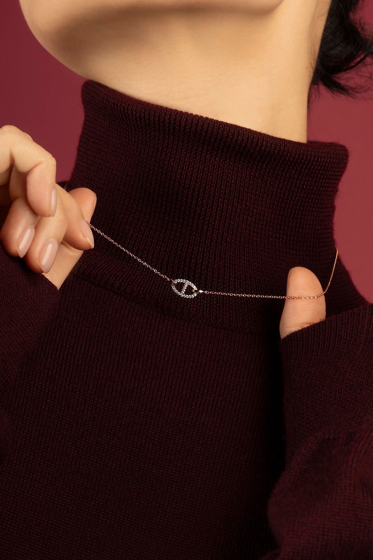Woman wearing APM Monaco necklace, a delicate rose glow against burgundy warmth.