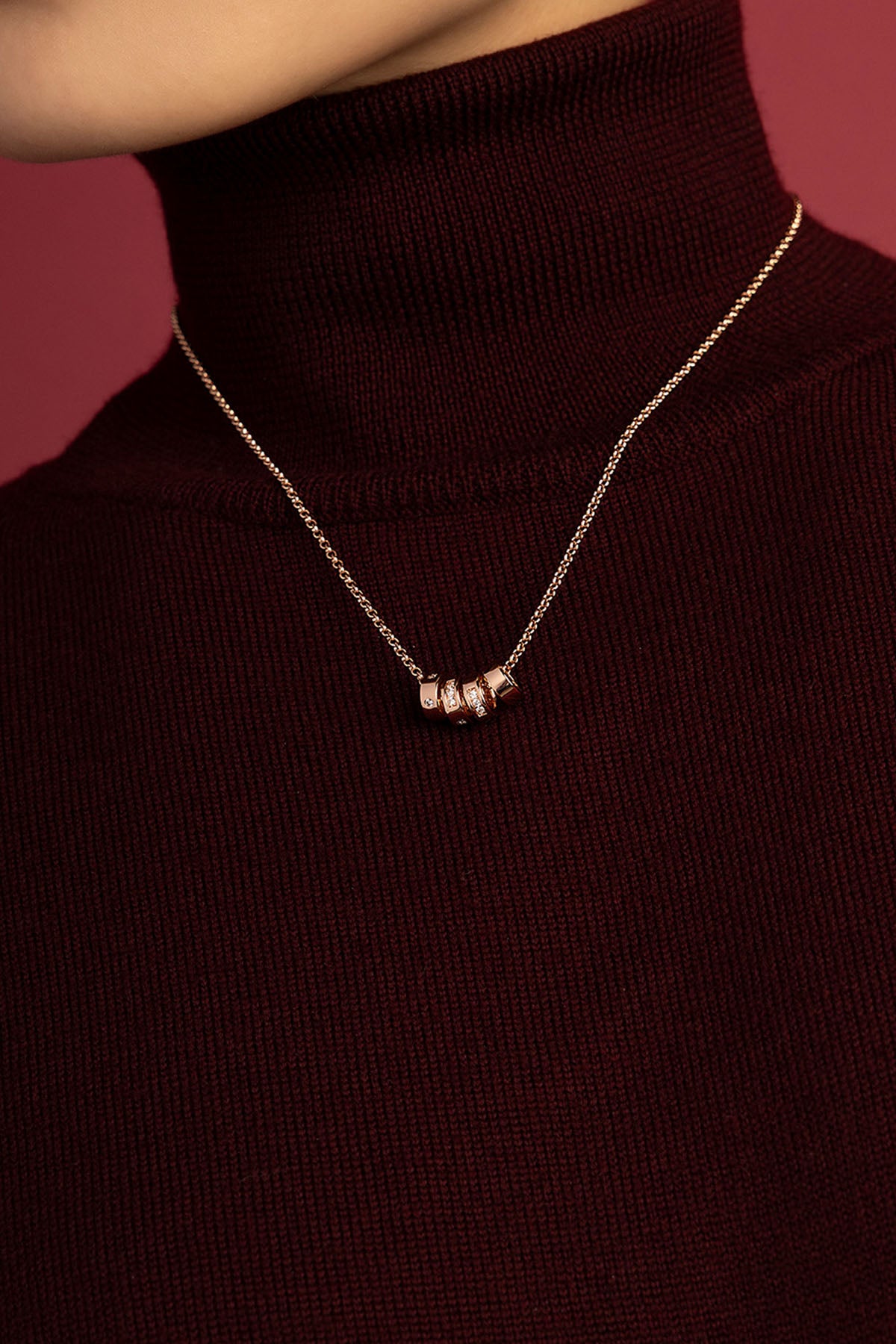 Woman wearing APM Monaco necklace, delicate charms glowing against burgundy warmth.