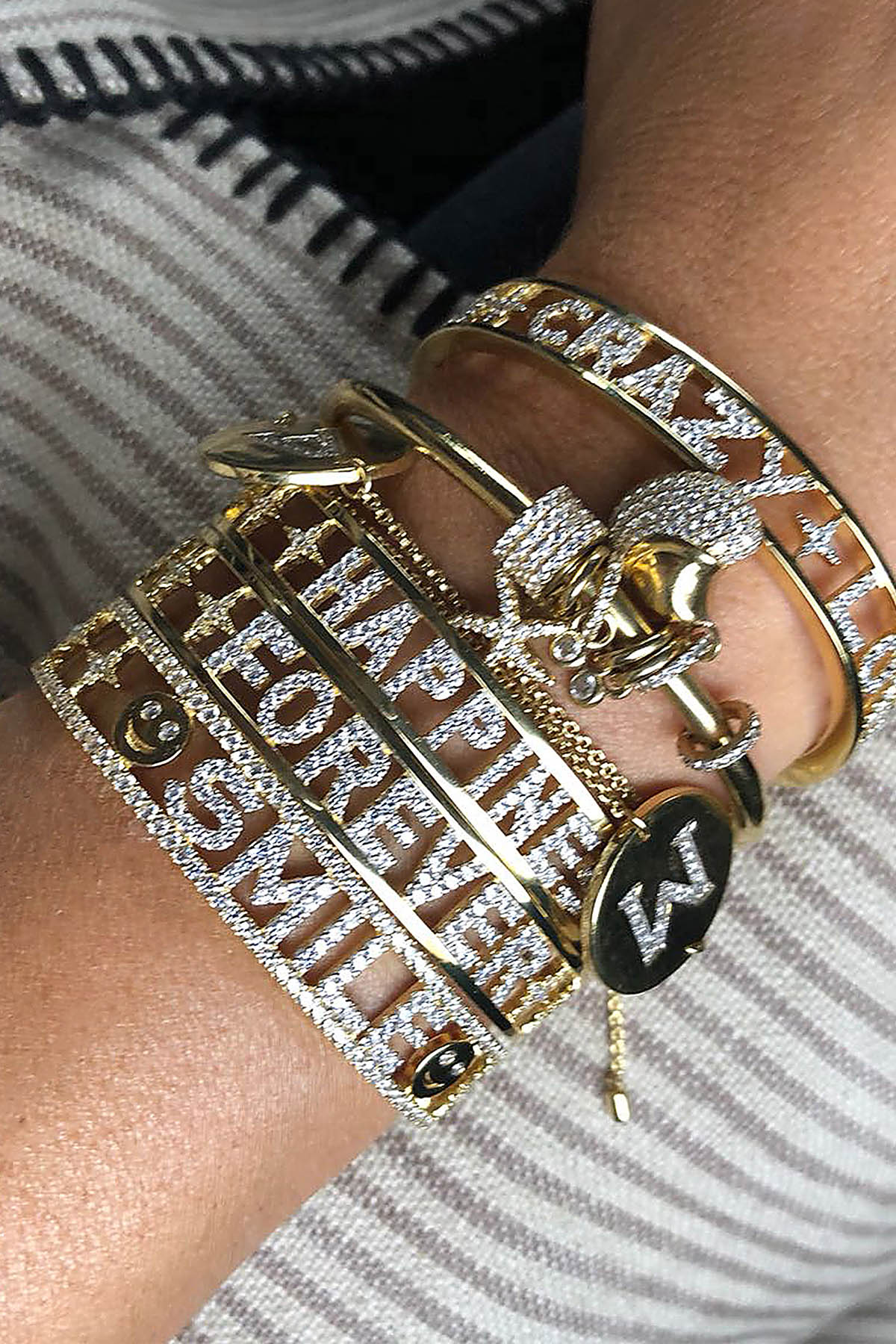 Woman wearing APM bracelet stack, a golden statement of joyful, sparkling words.
