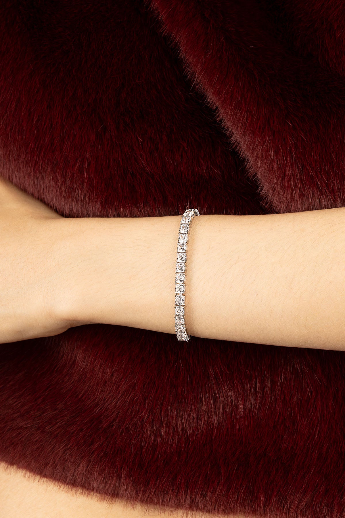 Woman wearing APM Monaco tennis bracelet, quiet sparkle against deep burgundy elegance.