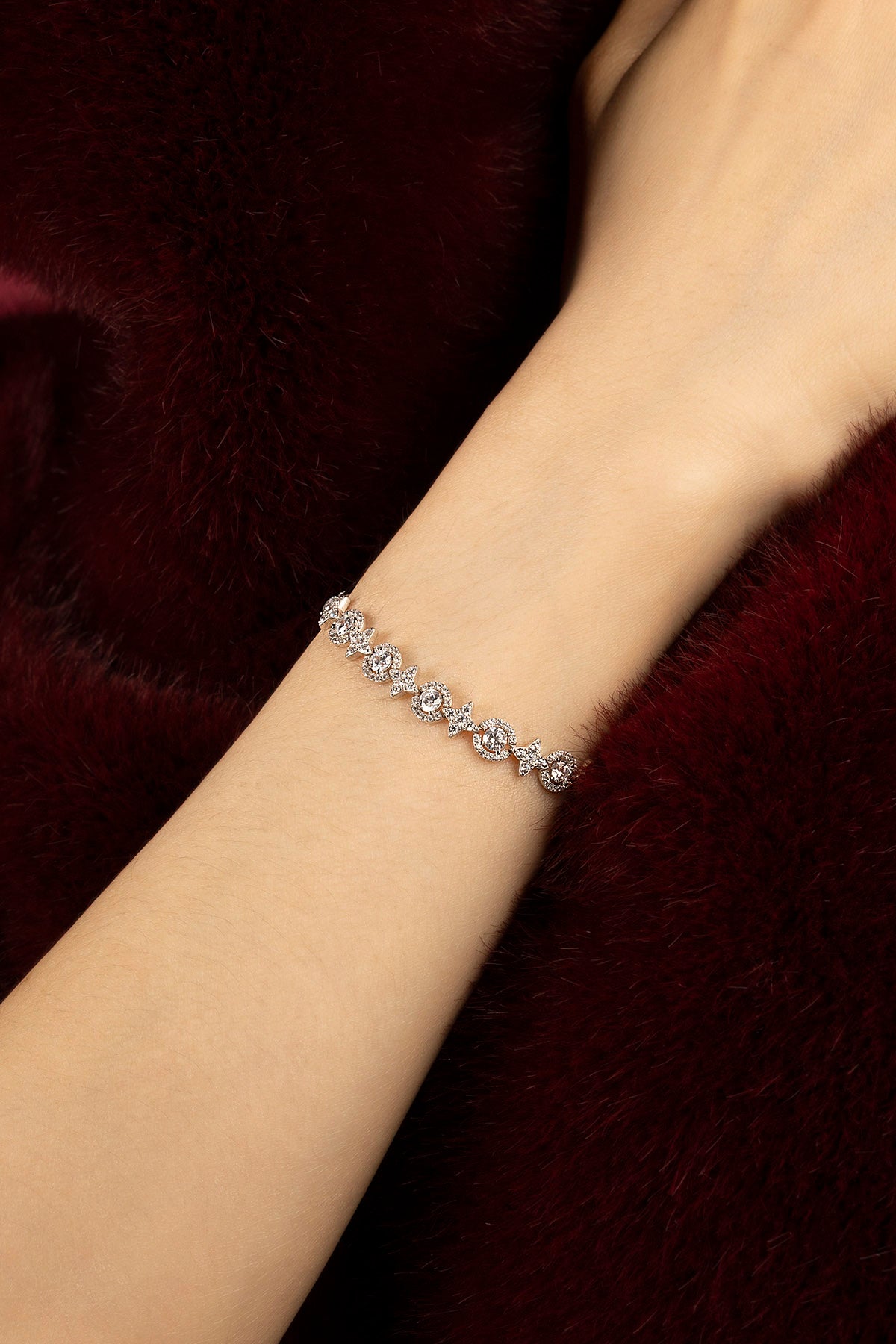 Woman wearing APM bracelet, a delicate sparkle against plush burgundy.