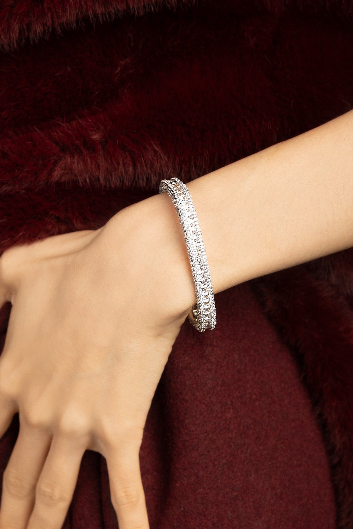 Woman wearing APM Monaco bangle, radiant sparkle against plush crimson elegance.