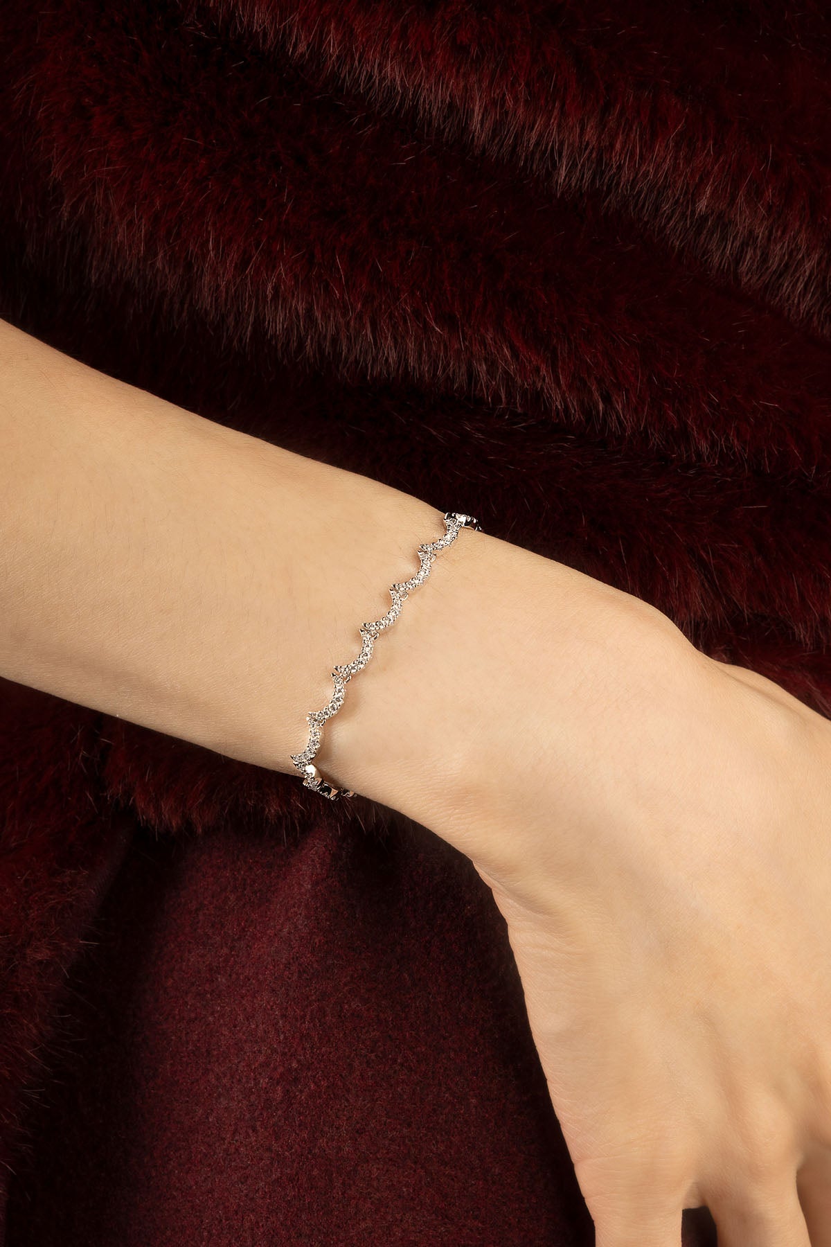 Woman wearing APM Bracelet, a shimmering wave of light against deep velvet.