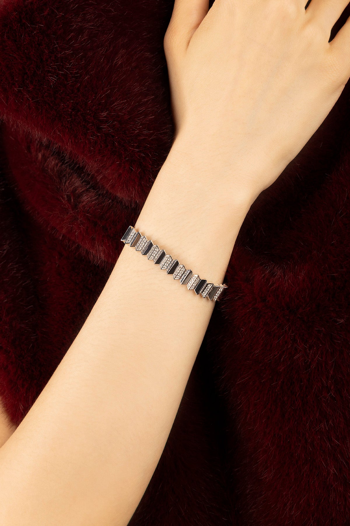 Woman wearing APM bracelet, a sharp geometric statement against plush burgundy.